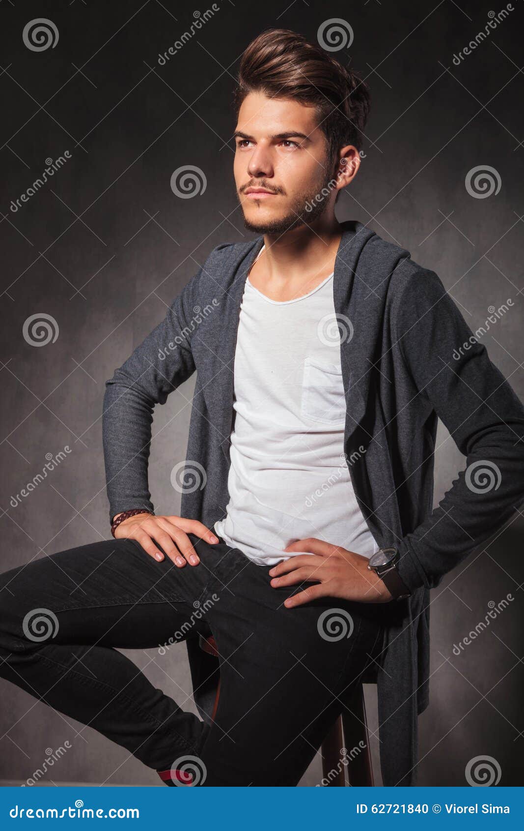 Young Man Sitting in Studio with Hands on Waist Looking Away Stock ...