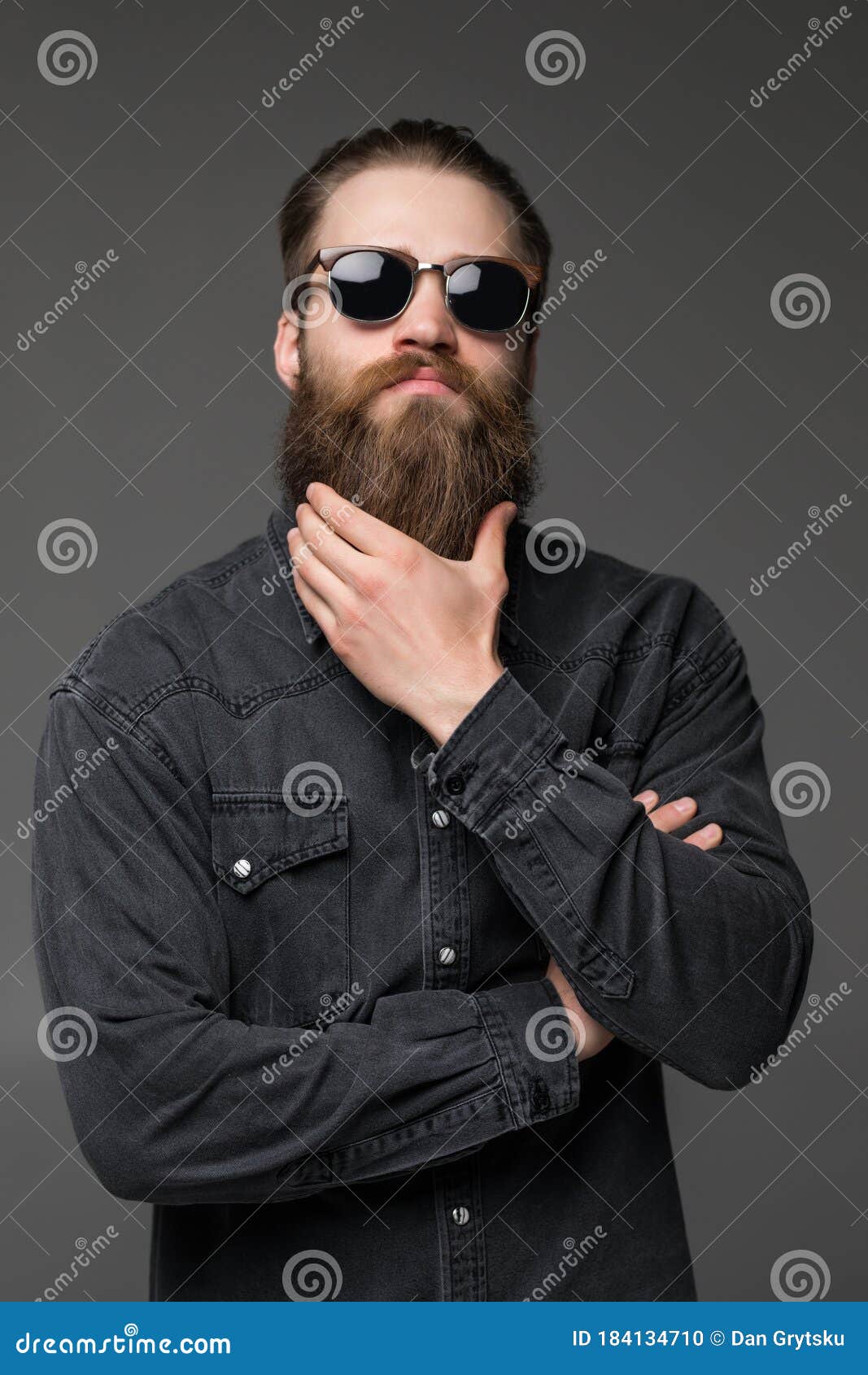 young handsome man in sunglasses touch his long beard  on gray background