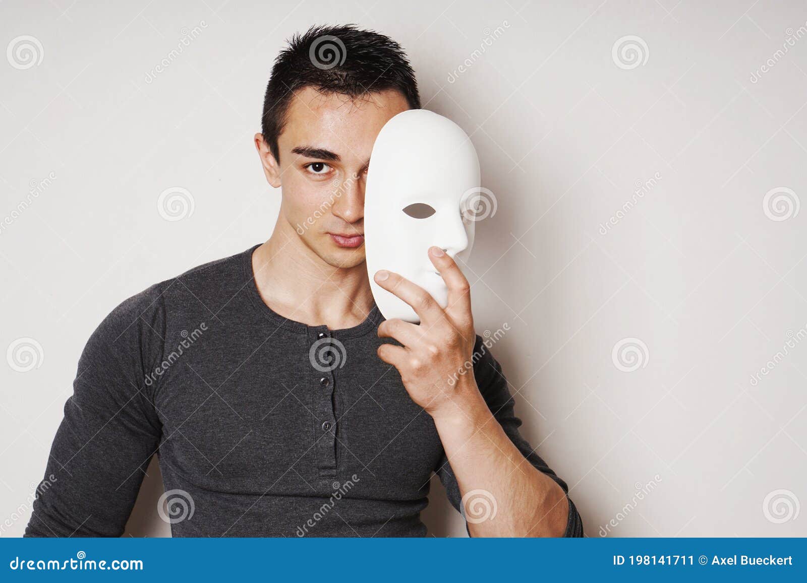 Young Man Taking Off White Mask Revealing Face and Identity Stock