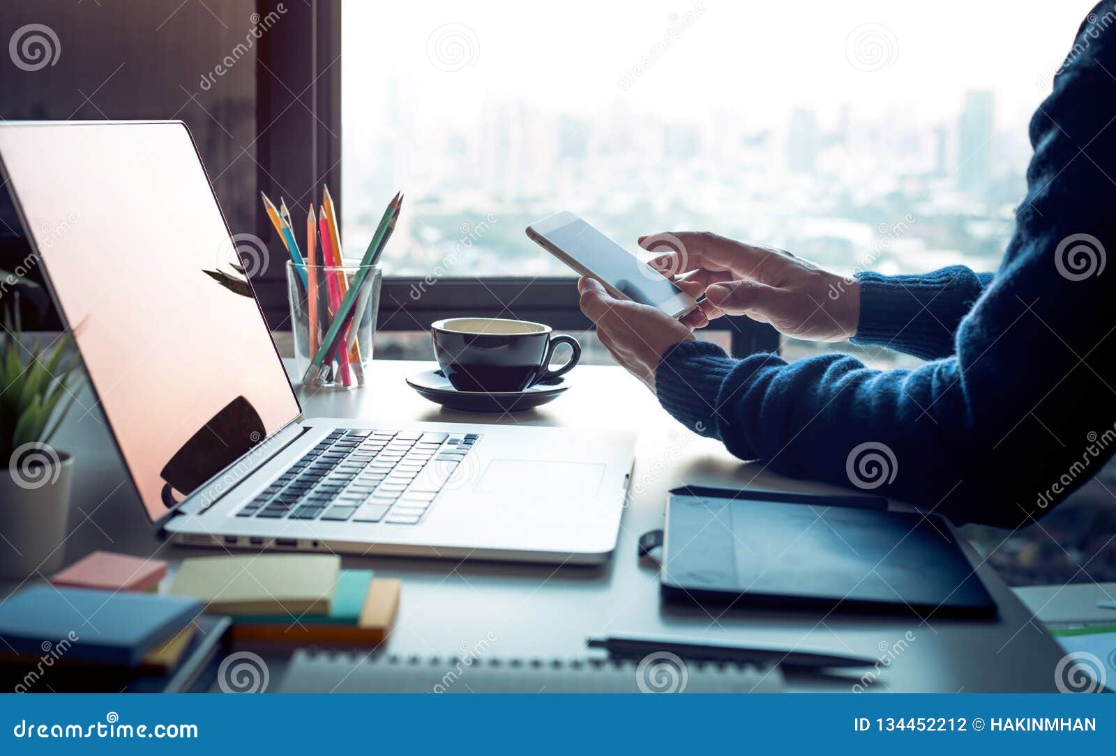 young man using smartphone with modern work table and computer laptop and cityscapes view from window.business  ideas.