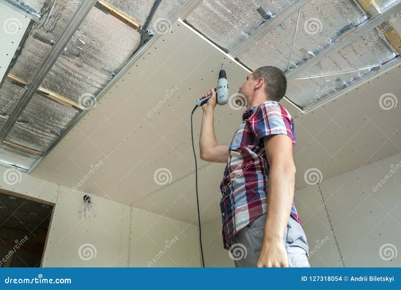 Young Man In Usual Clothing And Work Gloves Fixing Drywall