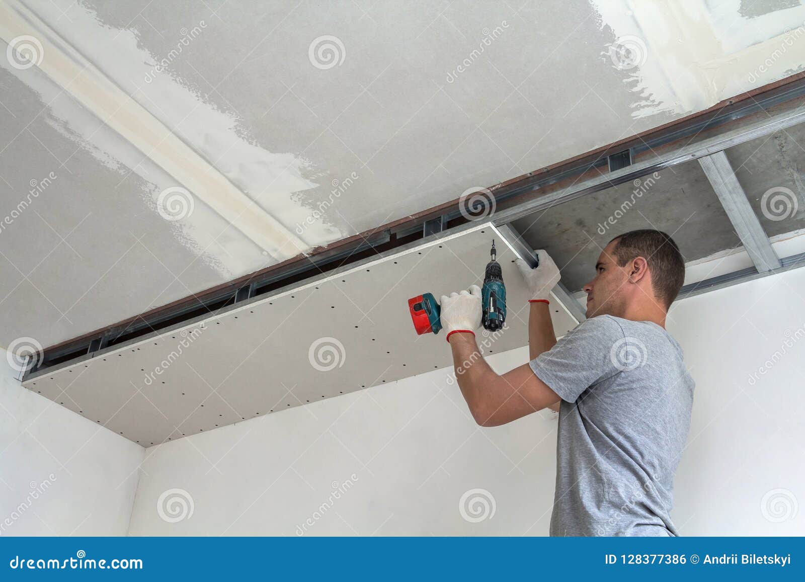 Young Man In Usual Clothing And Work Gloves Fixing Drywall