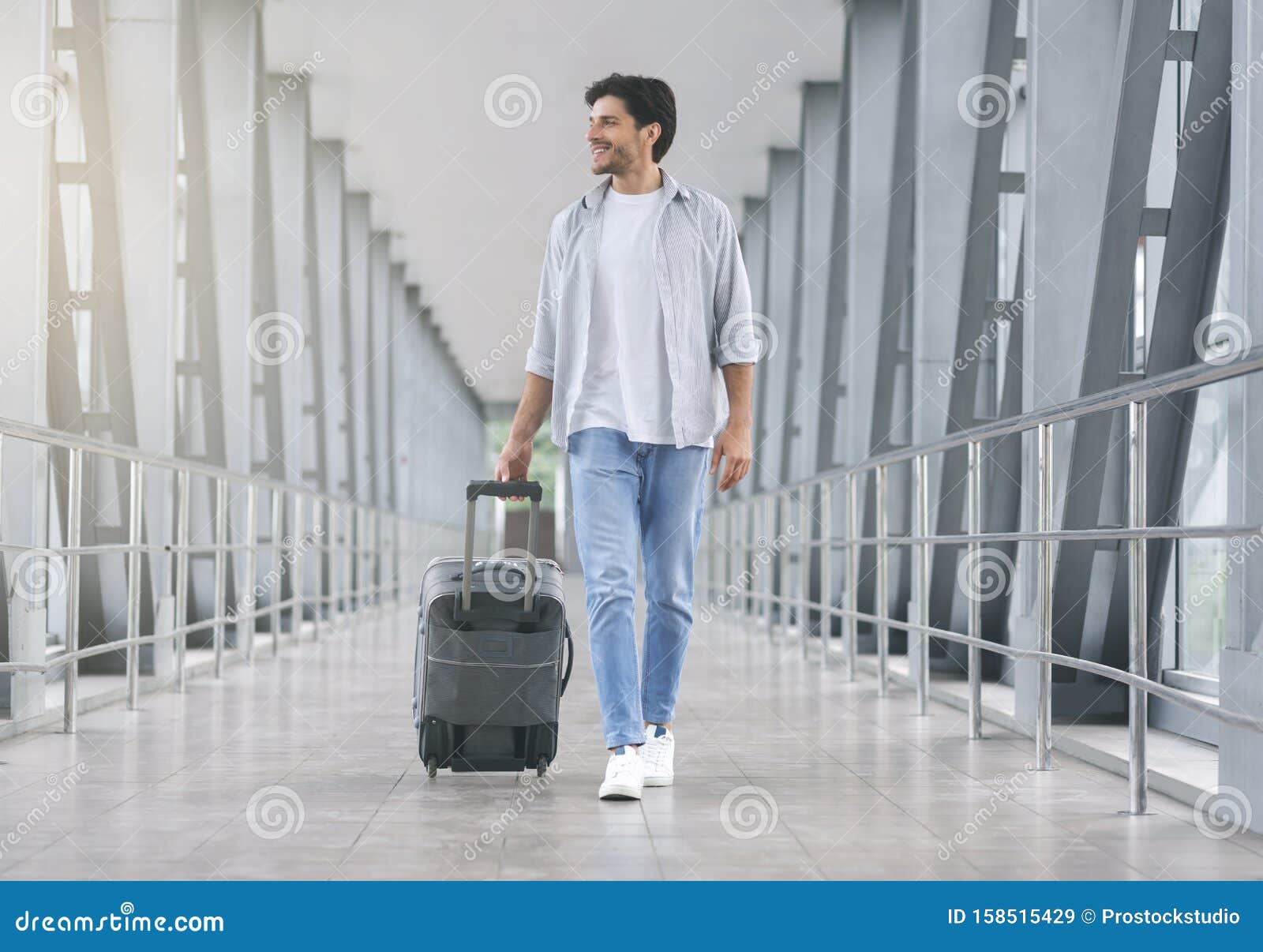 young man walking in airport walkway with luggage