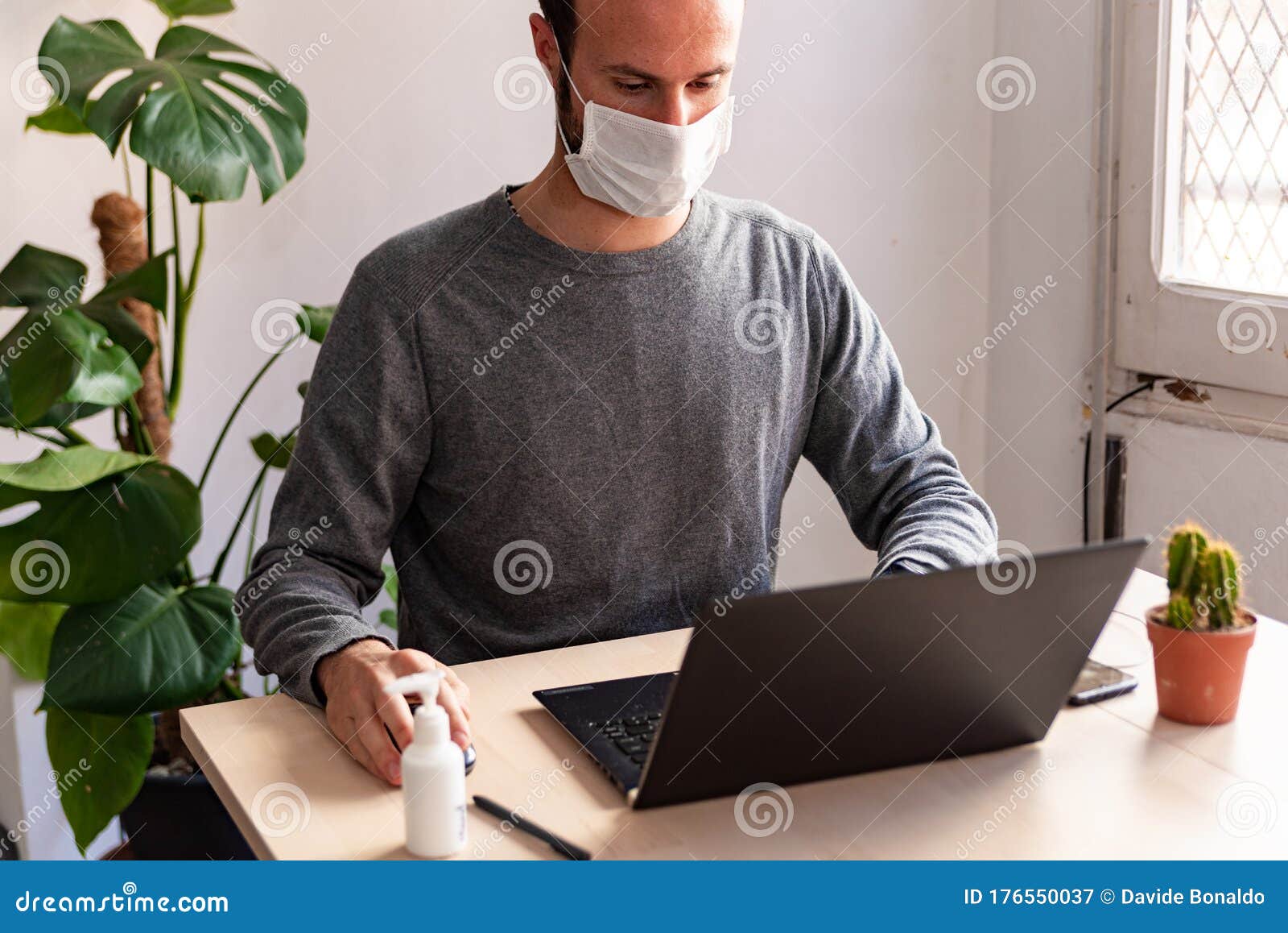 young man wearing medical face mask at work from home due to corona virus outbreak with laptop and mobile phone on wooden table,