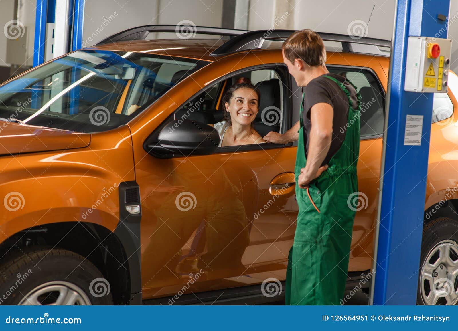 A Young Mechanic Communicates with a Client in an Orange Car Stock