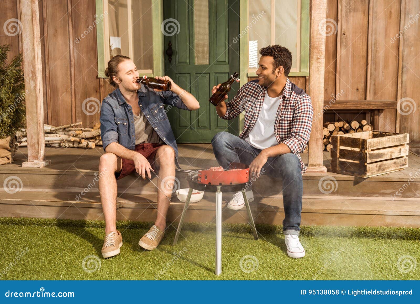 Young Men Drinking Beer and Preparing Meat on Outdoor Grill Stock Photo