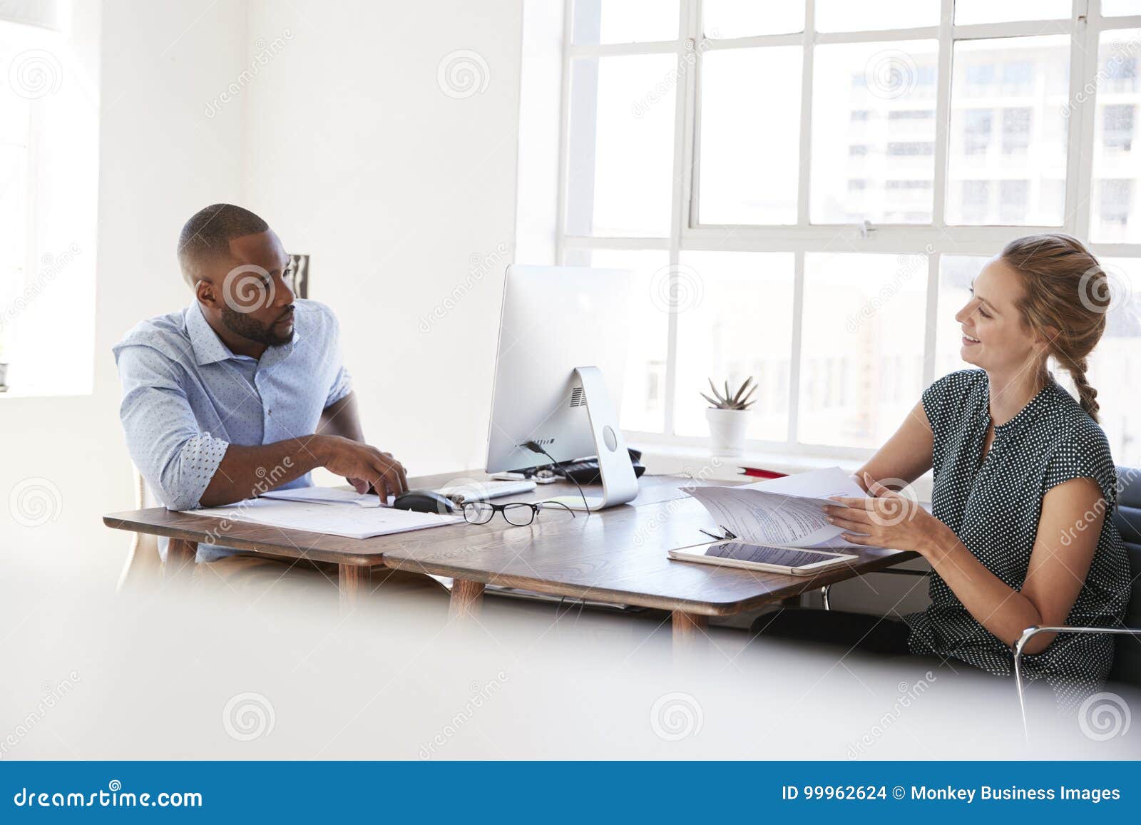 young man and woman talking across their desks in an office