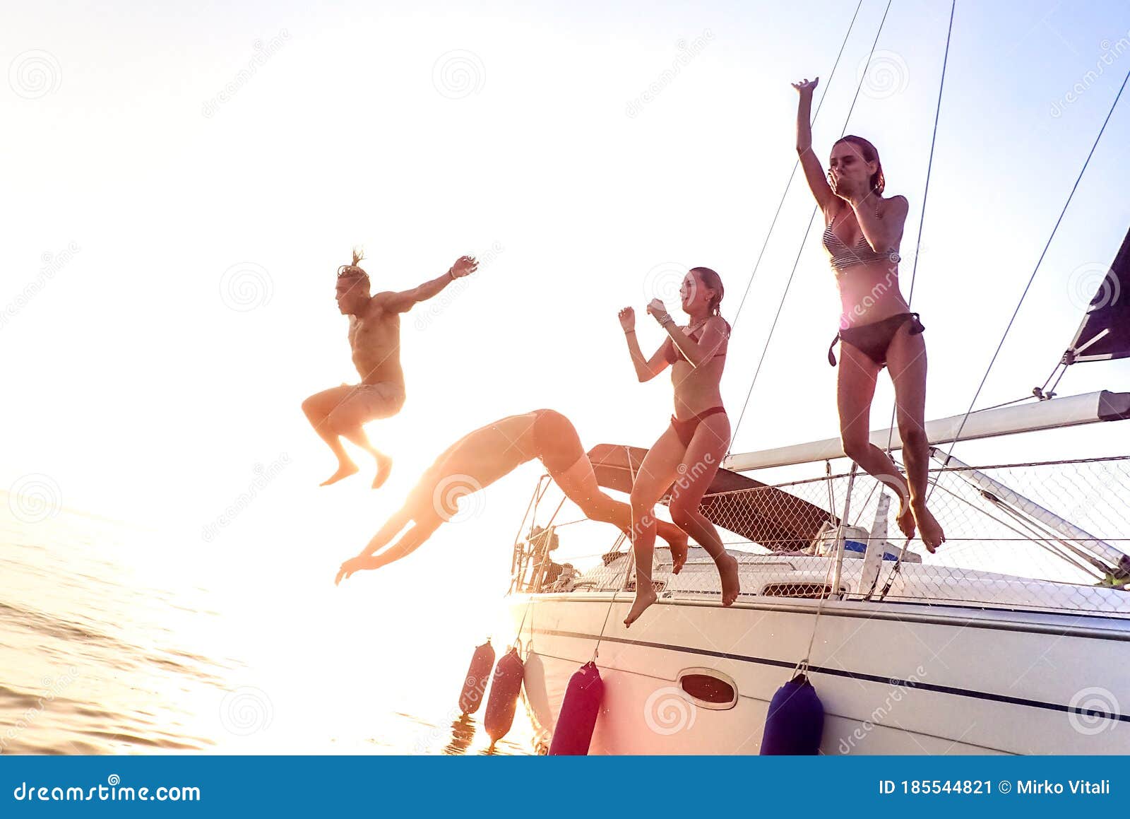 young millenial friends jumping from sailboat at sea ocean trip - guys and girls having summer fun together at sail boat party day