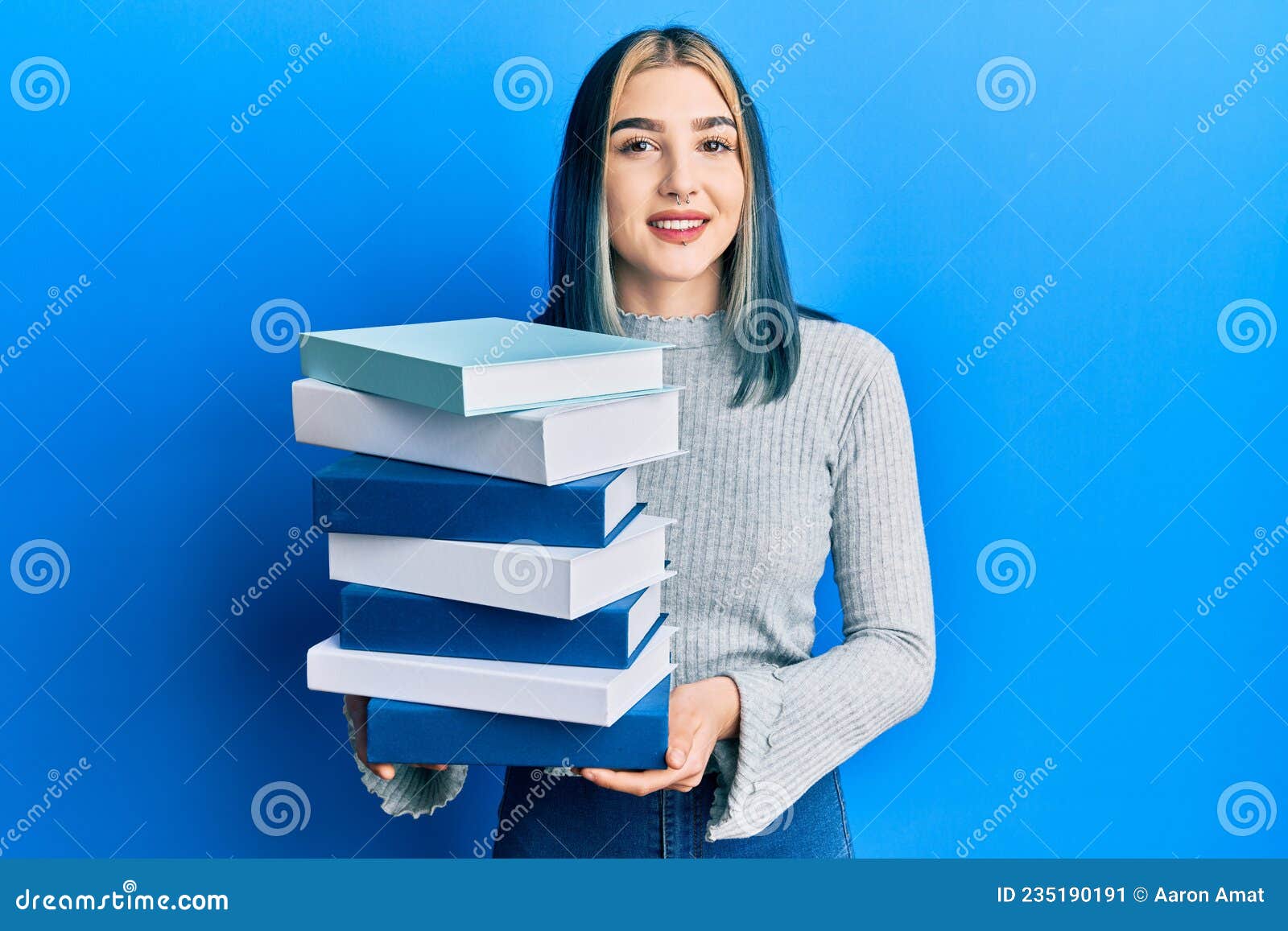 young modern girl holding a pile of books smiling with a happy and cool smile on face