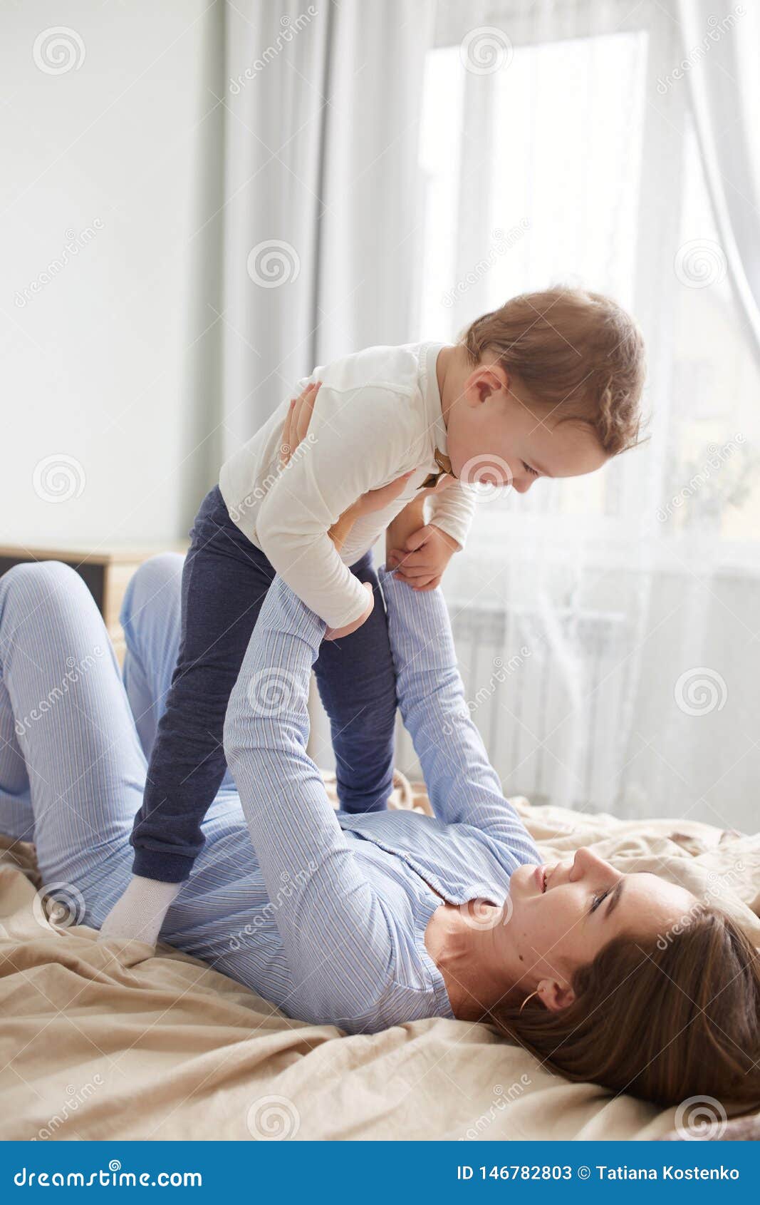 Young Mother Dressed in Light Blue Pajama Lays on the Bed with Beige ...