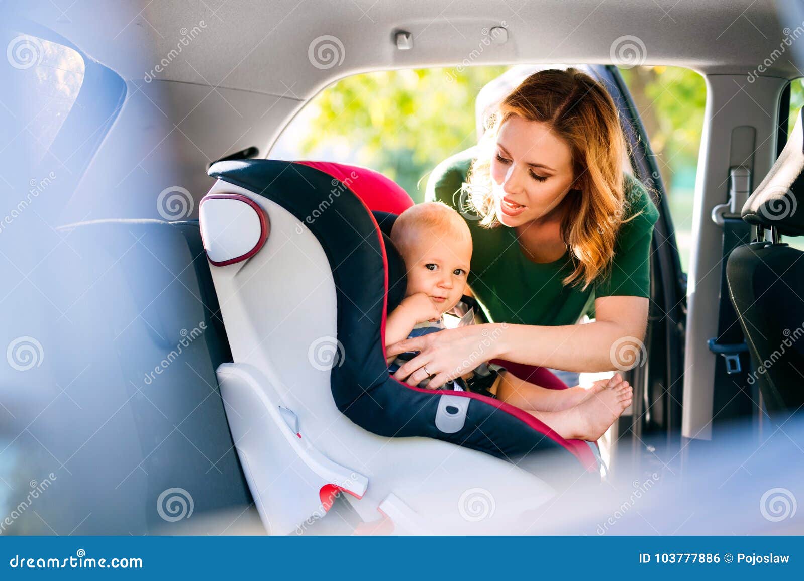young mother putting baby boy in the car seat.
