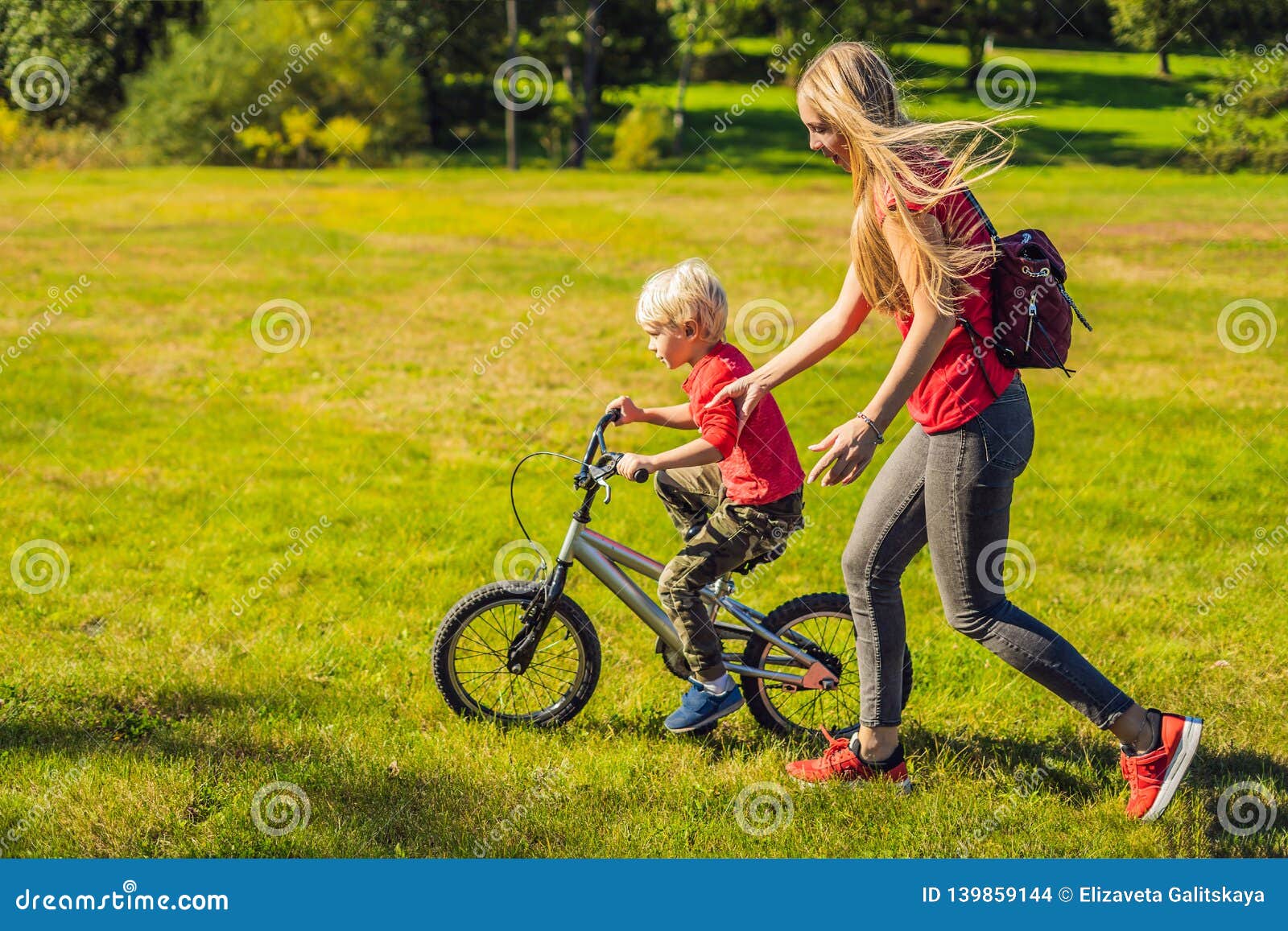 Young Mother Teaching Her Son How To Ride A Bicycle In The Park Stock ...