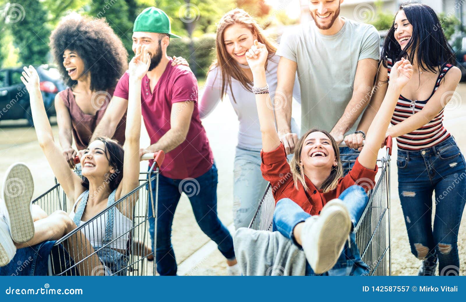 young multiracial people having fun together with shopping cart - millenial friends sharing time with trolleys at commercial mall