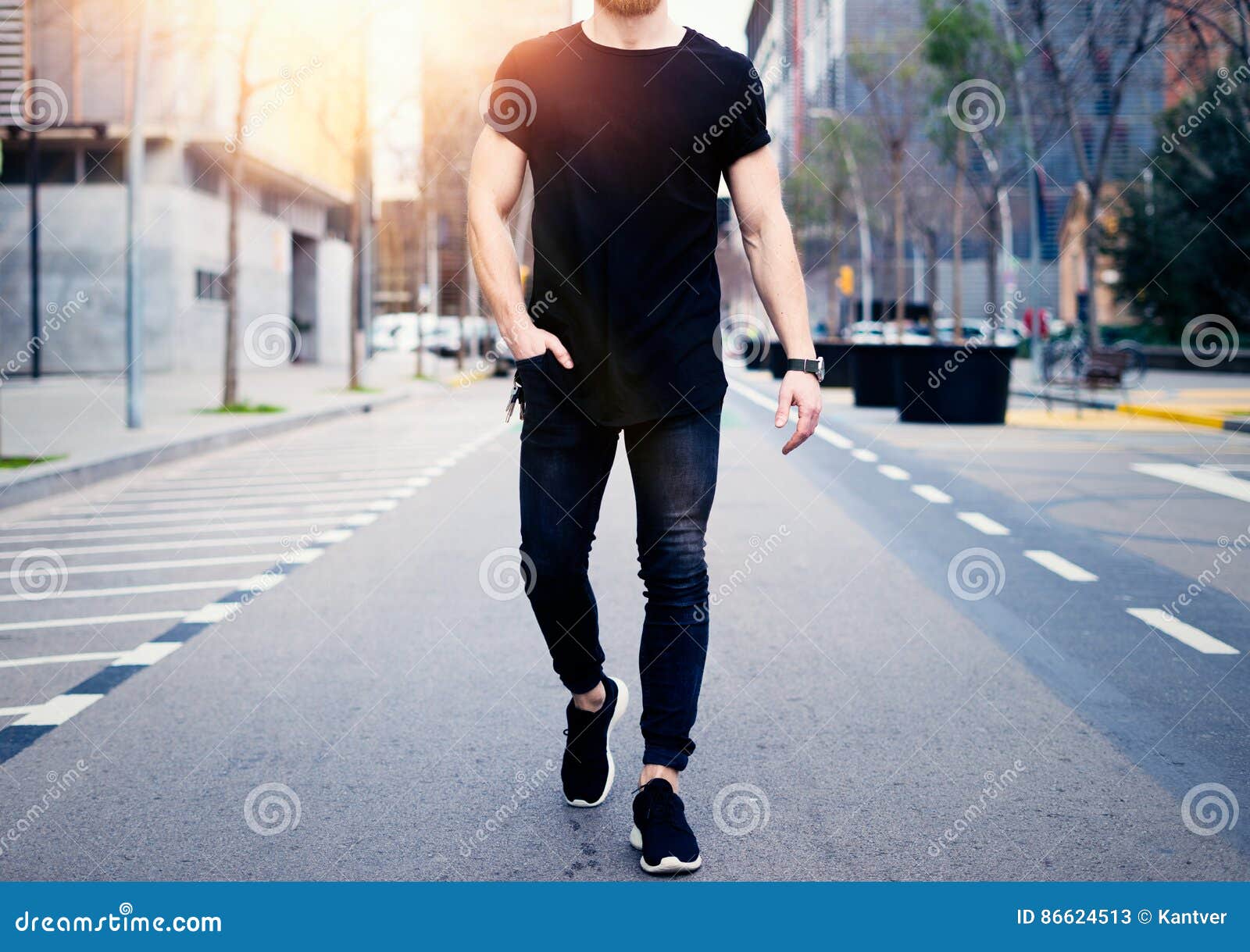young muscular man wearing black tshirt and jeans walking on the streets of the modern city. blurred background