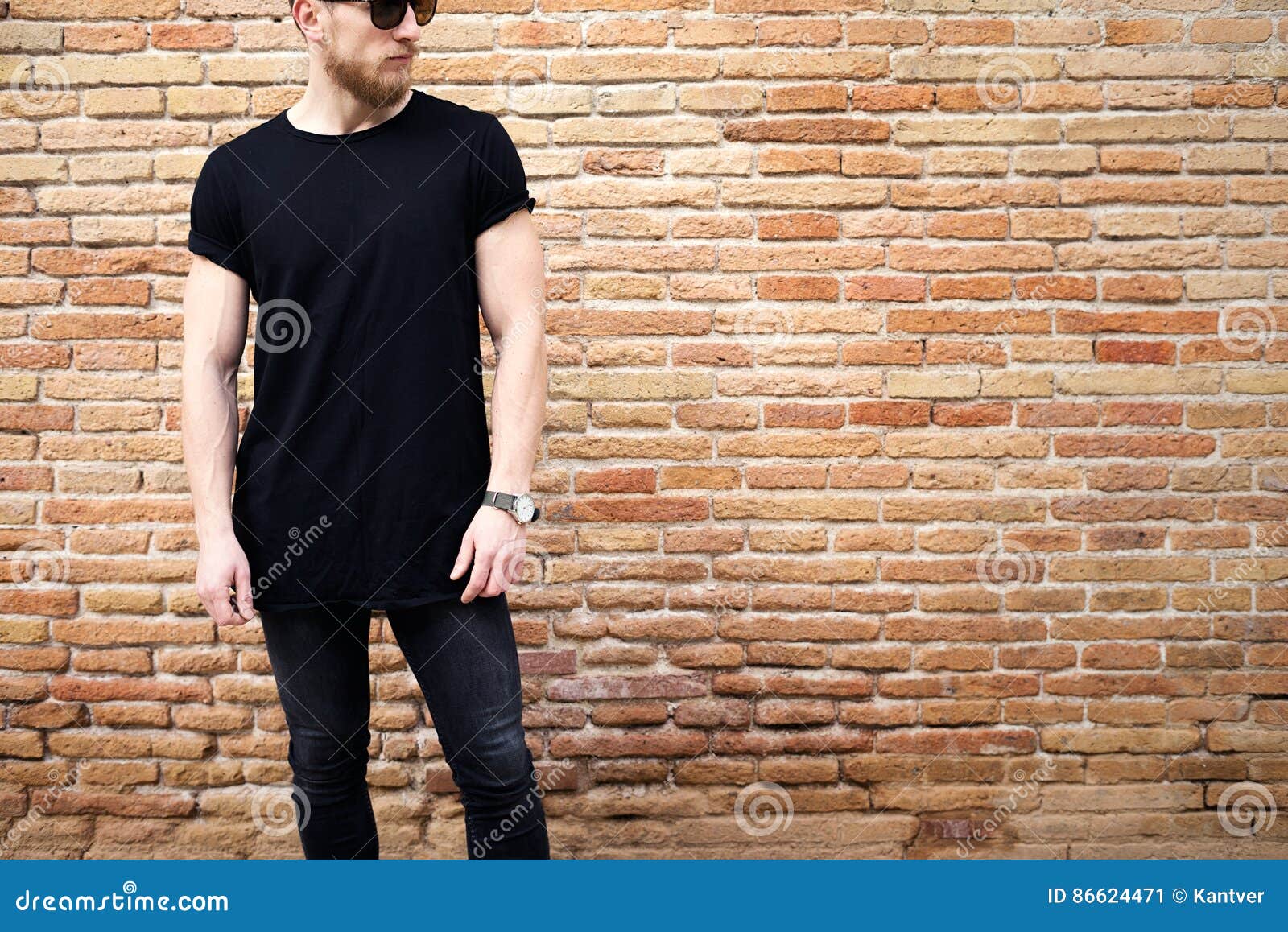 young muscular man wearing black tshirt,sunglasses and jeans posing outside. empty brown grunge brick wall on the