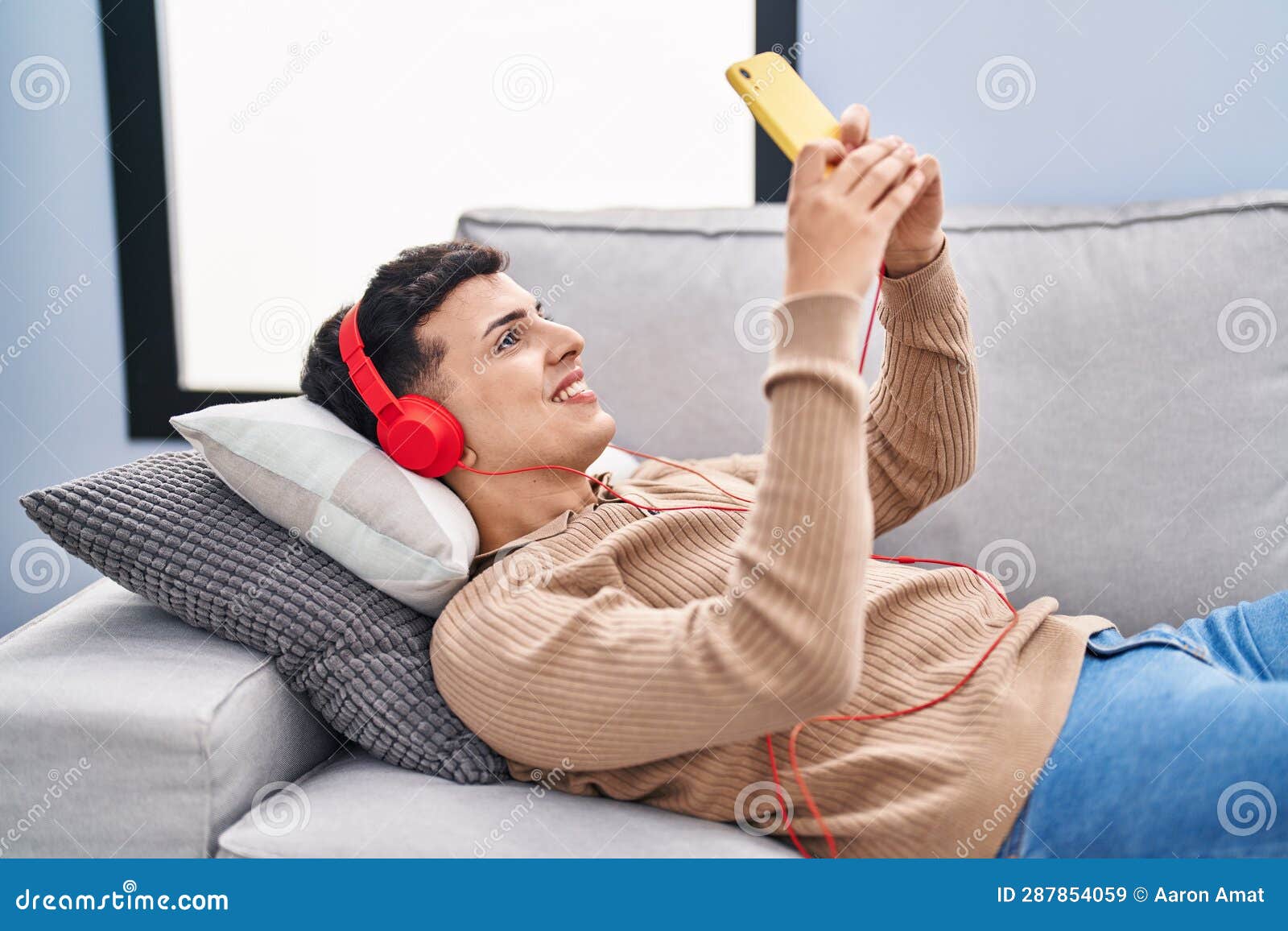 young non binary man listening to music lying on sofa at home