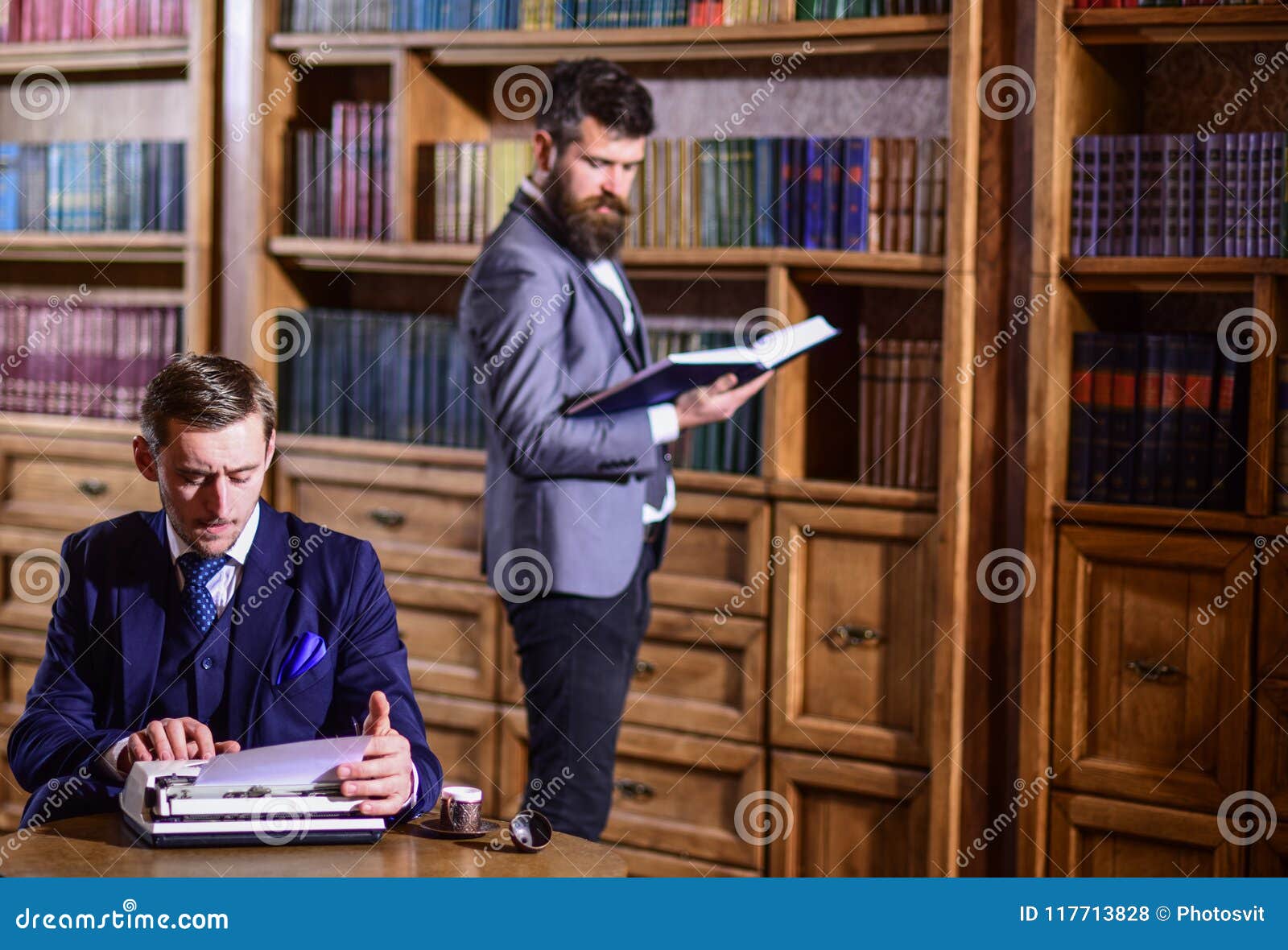 young oldfashioned writer with typewriter in library with bearded friend