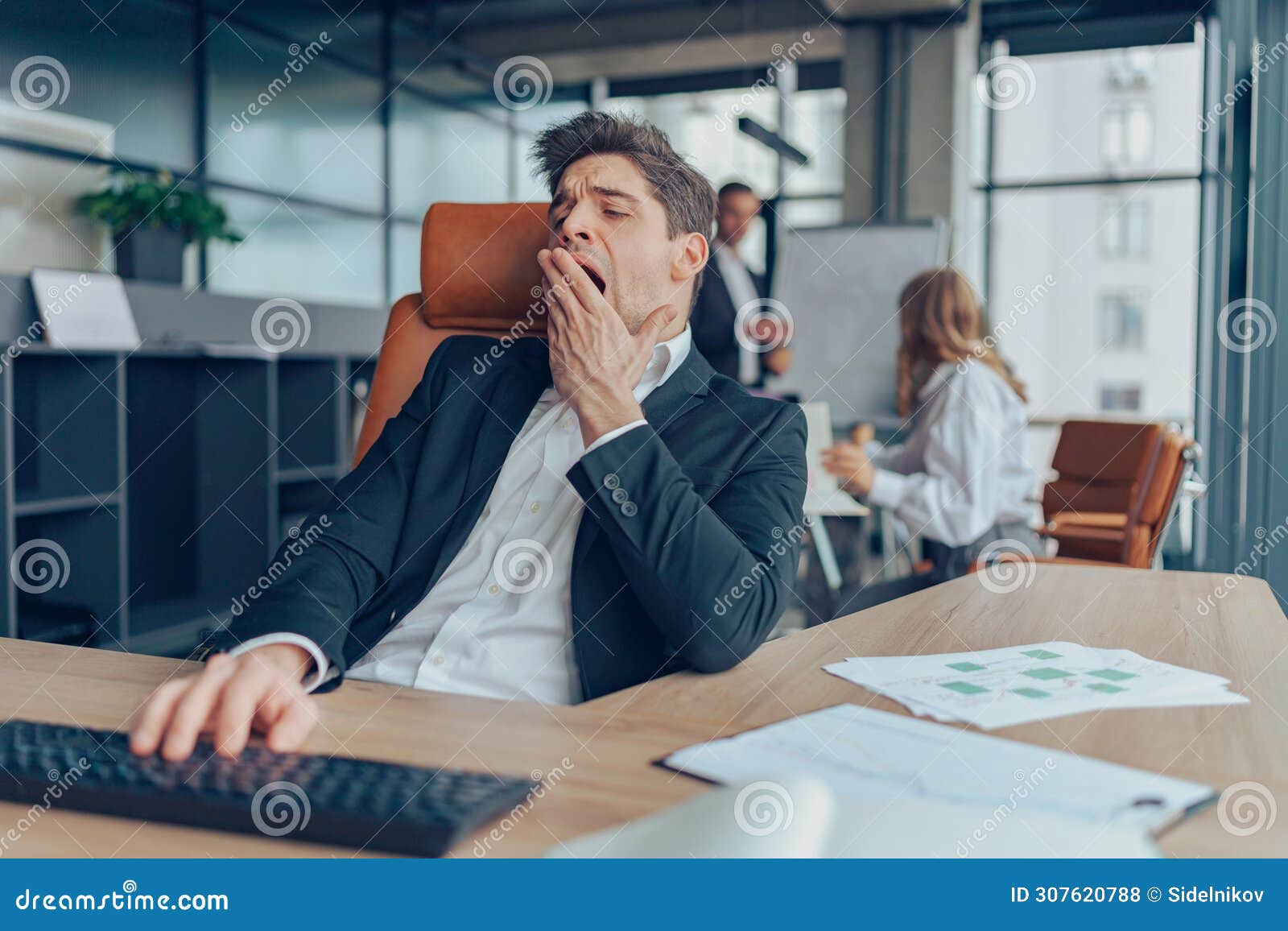 young overtired businessman yawning while working inside modern office with computer