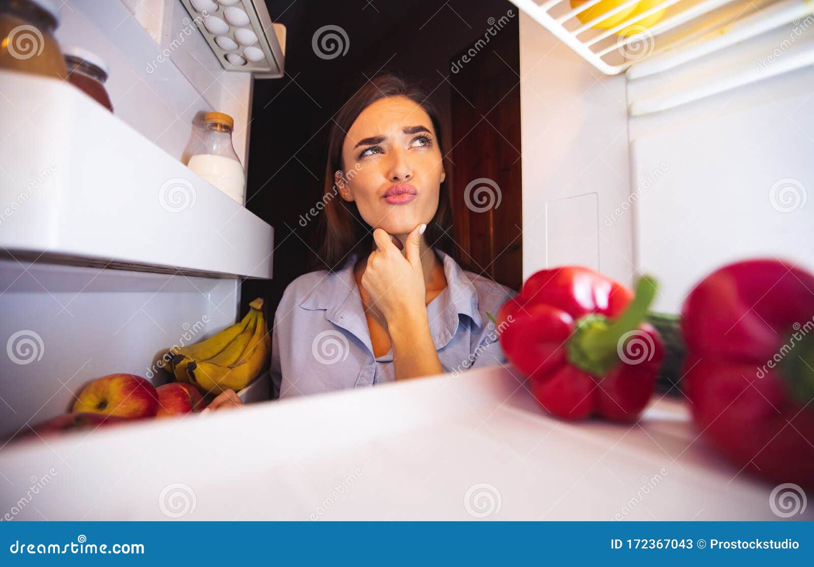 young pensive woman thinking near opened fridge