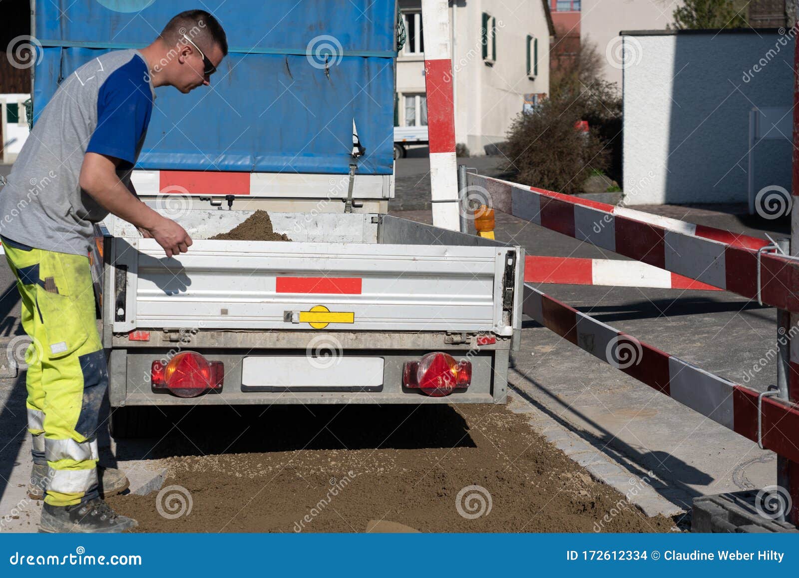 Young Pipeline Technician on Construction Site Closes Tailgate of a Trailer Loaded with Sand
