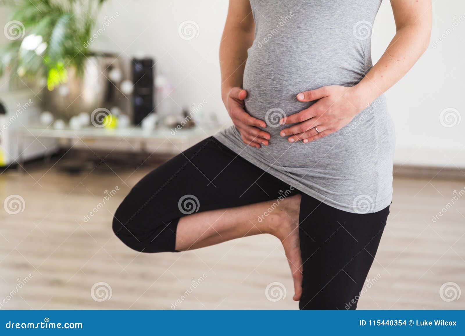 young pregnant woman standing in tree pose doing prenatal yoga holding belly