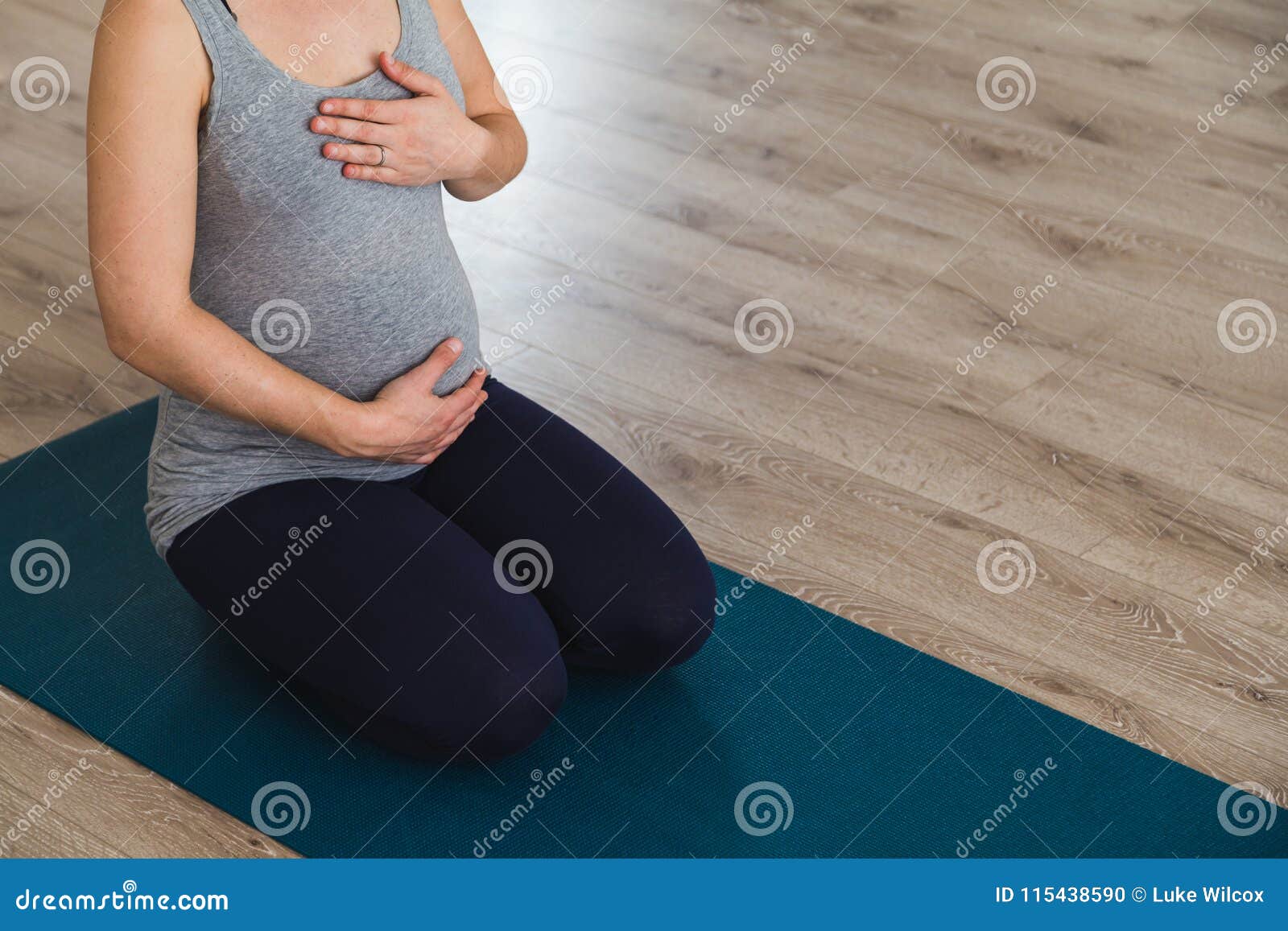 young pregnant woman sat on mat doing prenatal yoga holding belly