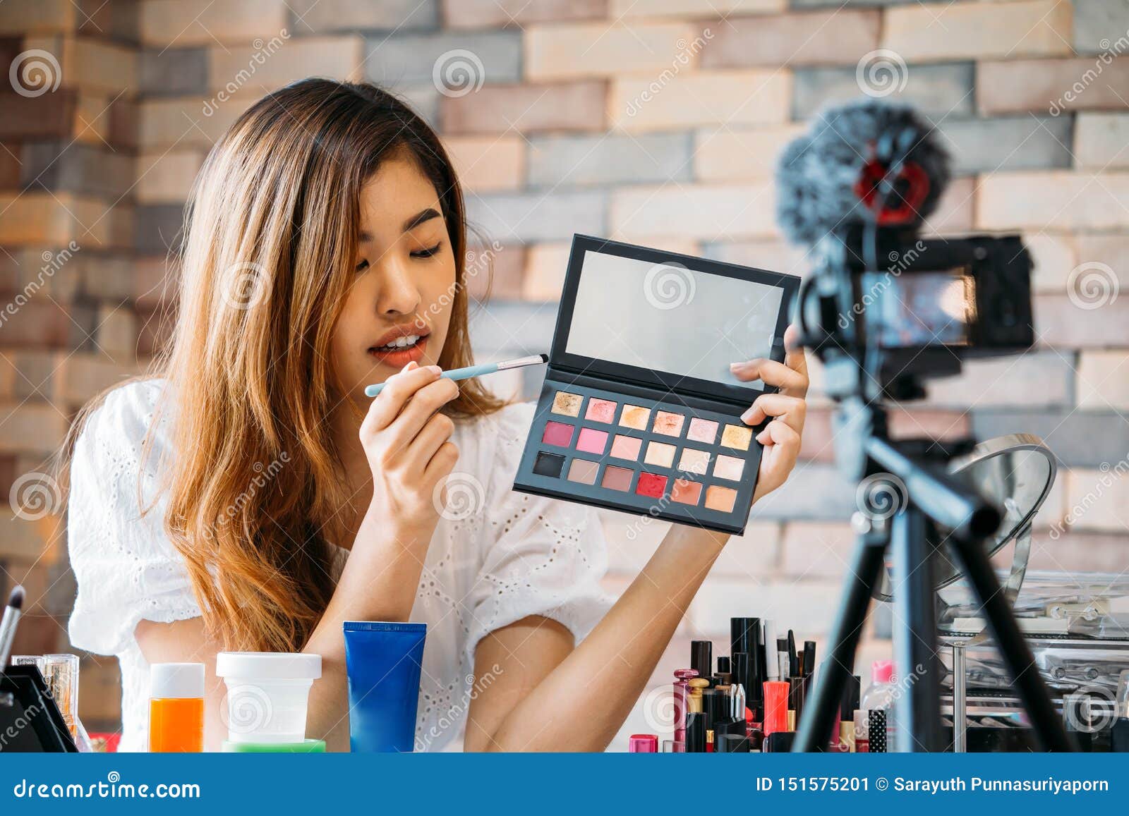 pretty asian woman recording makeup tutorial video about cosmetics with mobile phone on tripod
