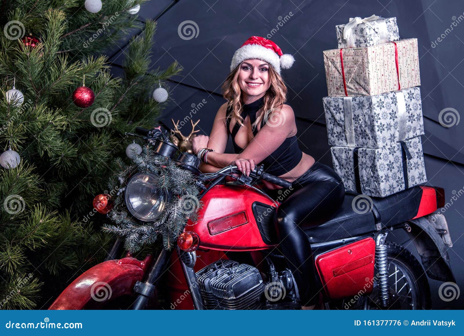 Young pretty girl in santa hat sits on a red motorcycle in Christmas decor with gift boxes
