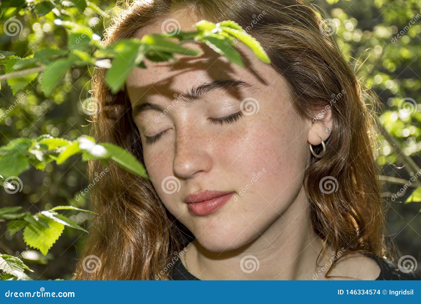 young red-haired caucasian woman with freckles with close eyes into a forest.