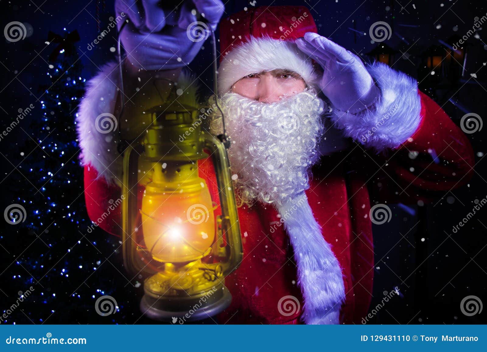 young santa clause, carrying lantern looks through blizard of snow with christmas tree and street lamp in background