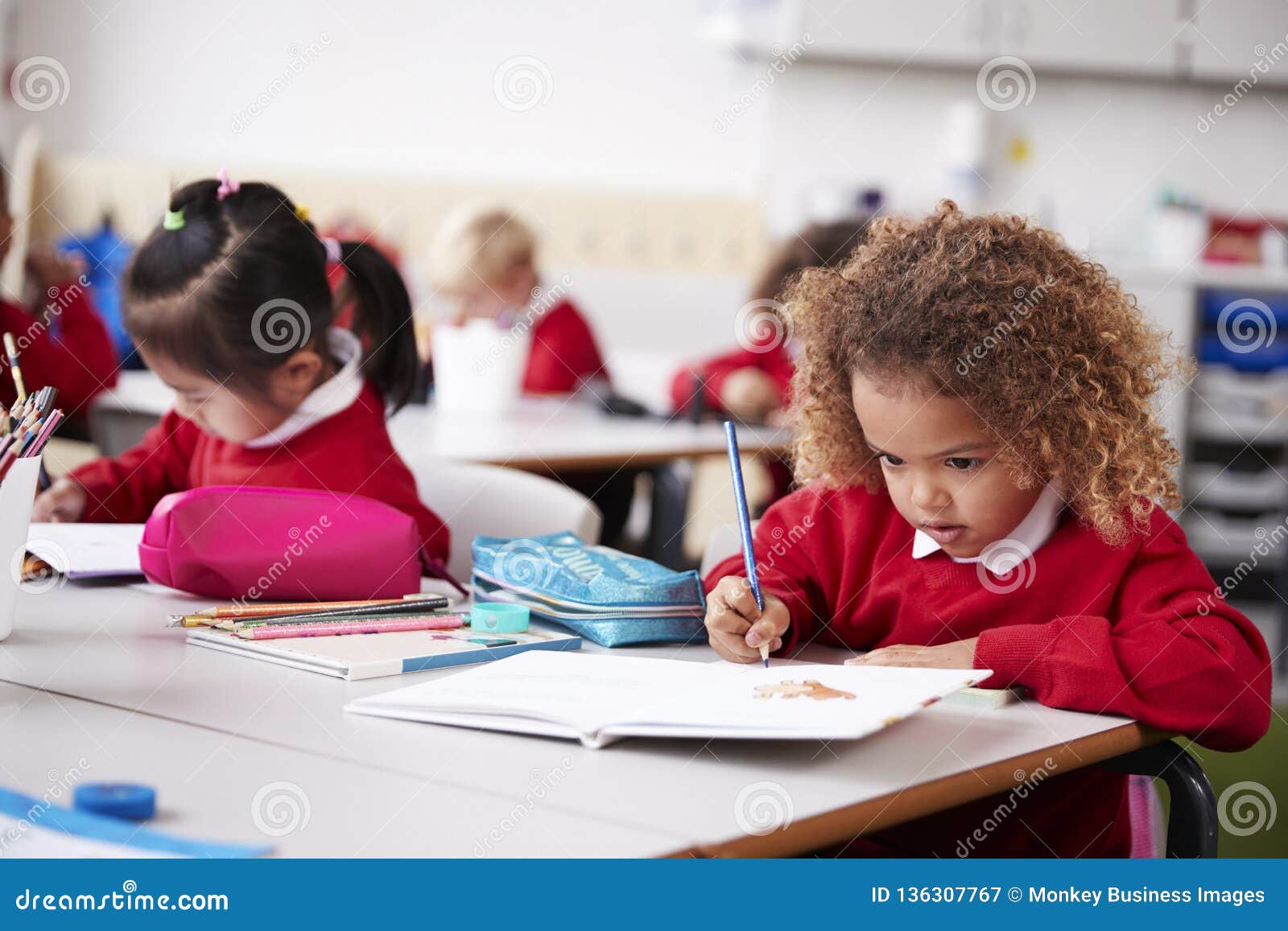 young schoolgirl wearing school uniform sitting at a desk in an infant school classroom drawing, close up