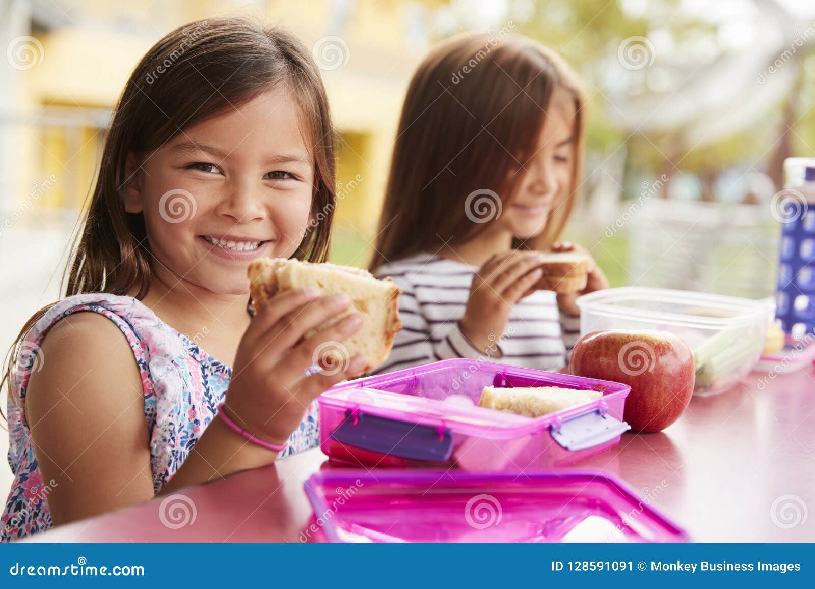 young schoolgirls holding sandwiches at school lunch table