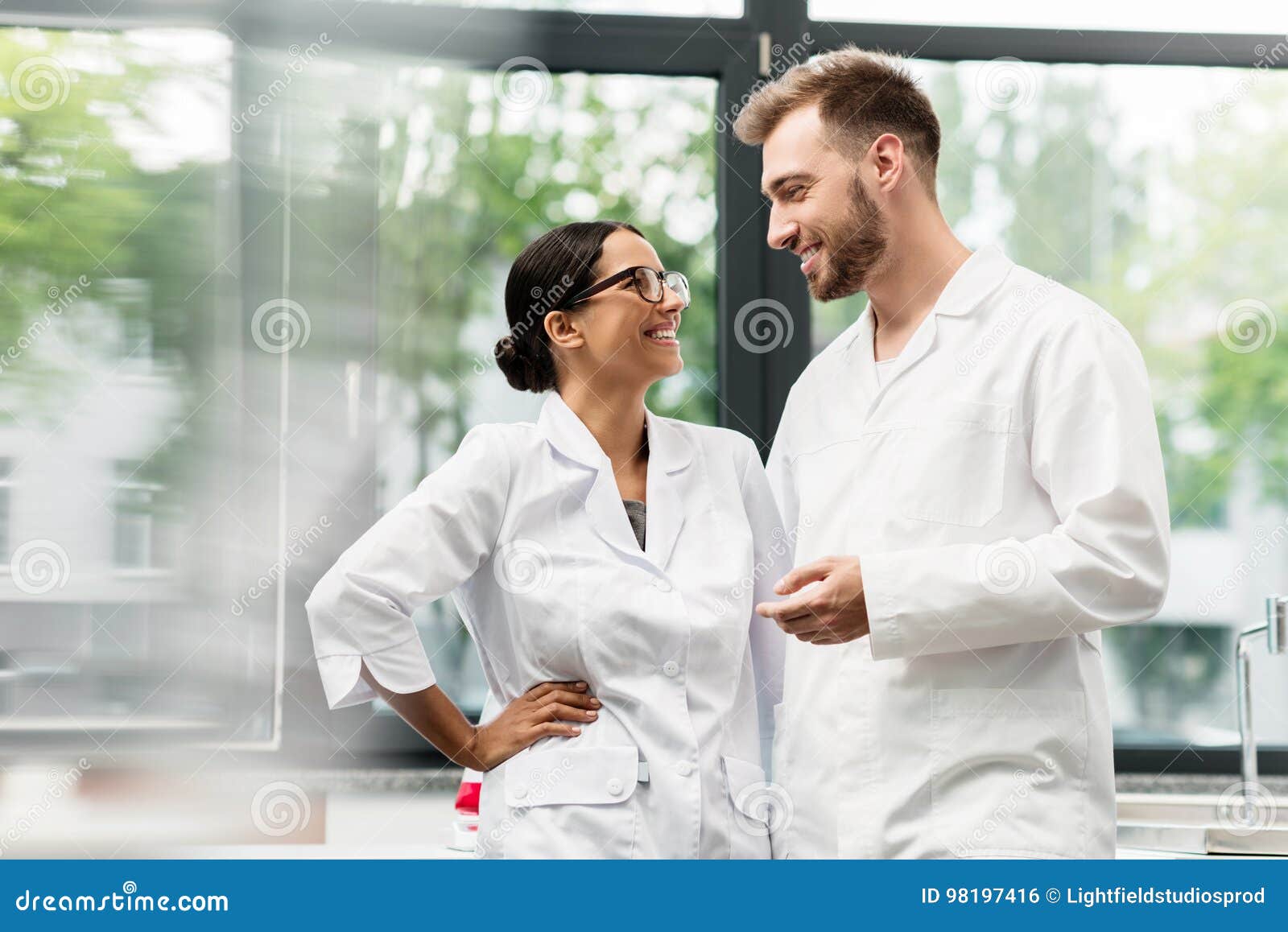 Young Scientists in White Coats Smiling Each Other in Lab Stock Photo