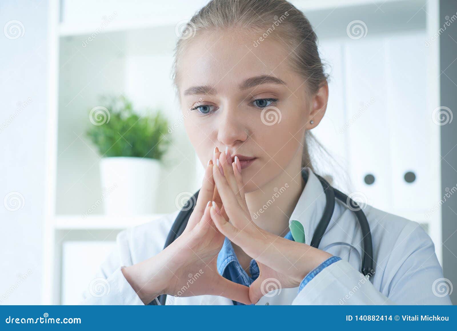 Young Serious Blonde Doctor Woman Sitting In Medical Office With Hands