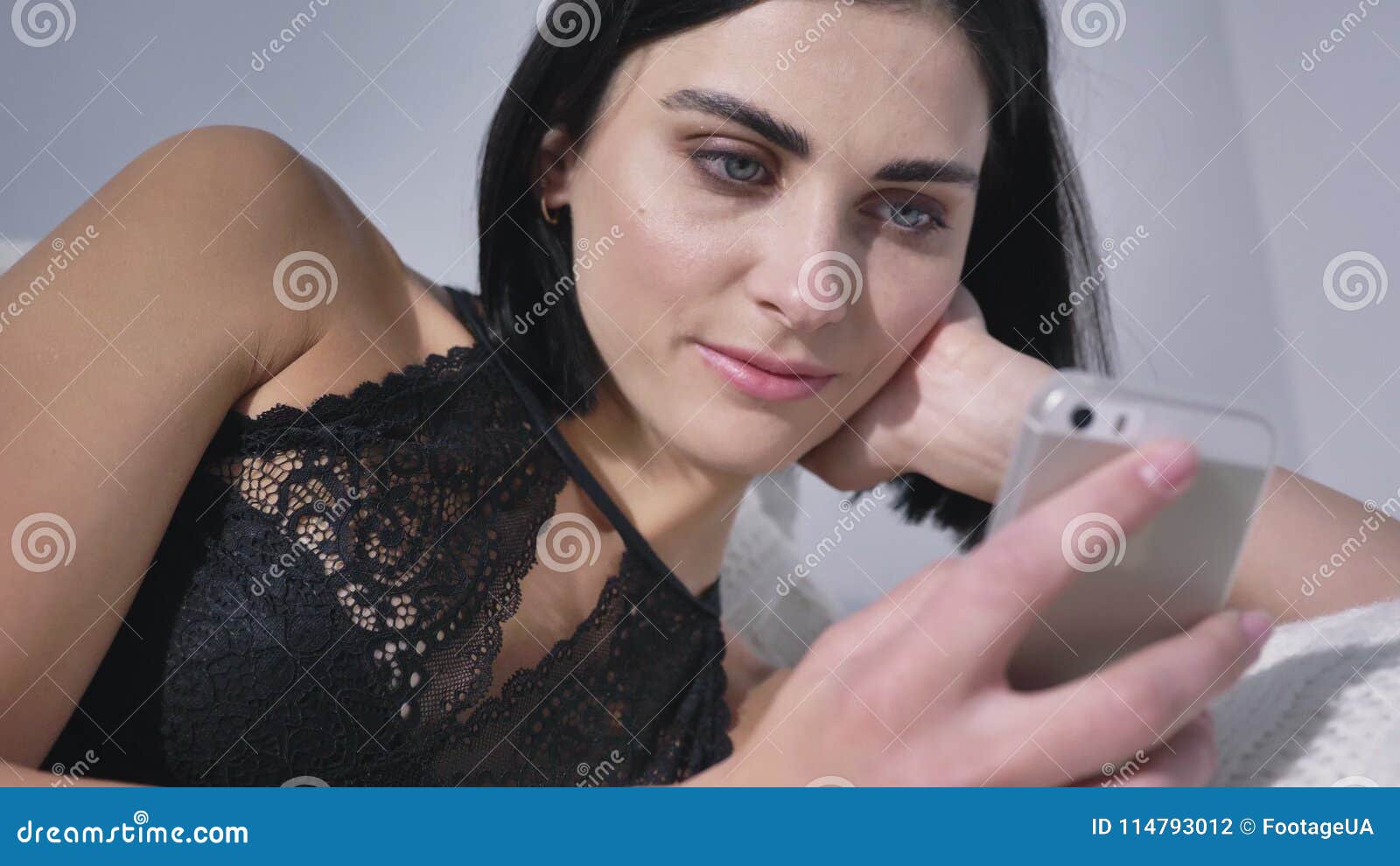Young Caucasian Brunette In Black Lingerie Using Smartphone Lying On Couch Smiling Daylight