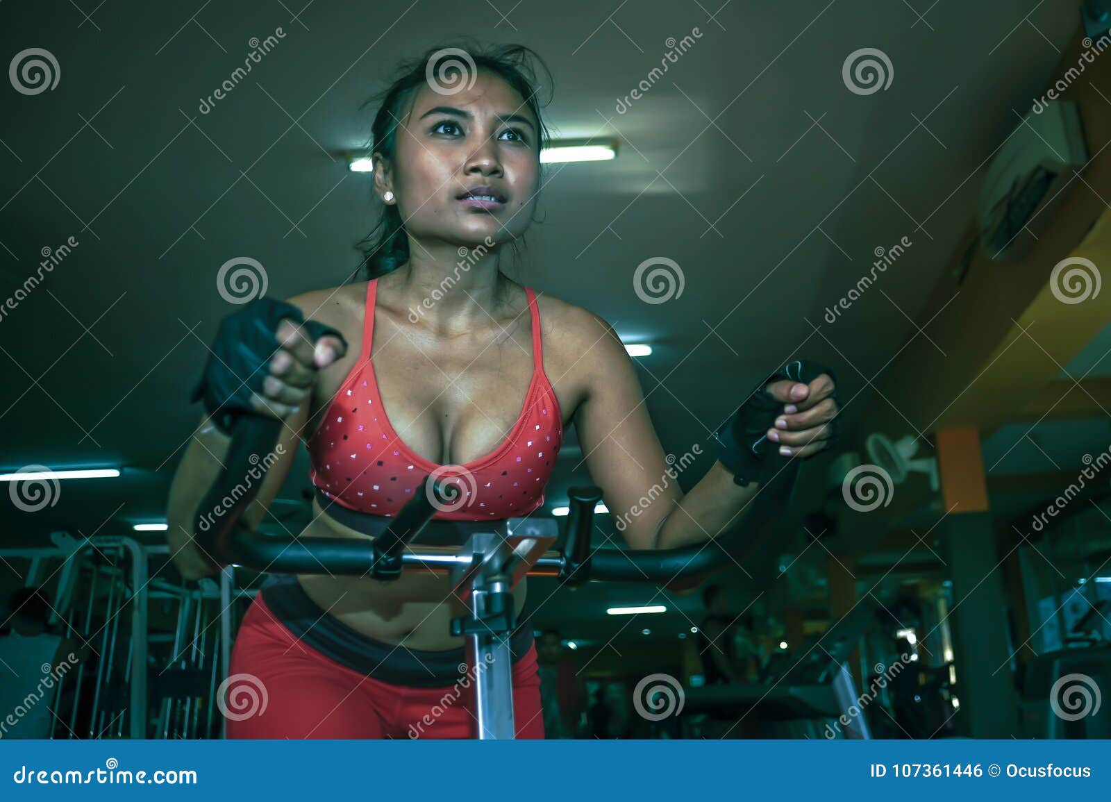 young and sweaty asian woman training hard at gym using elliptical pedaling machine gear in intense workout exercise