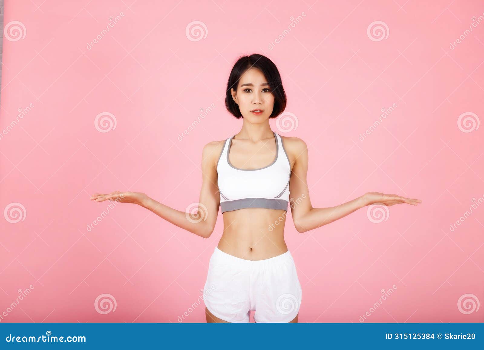 young slim fitness asian woman in white sportwear shows something on her palms  on pink background