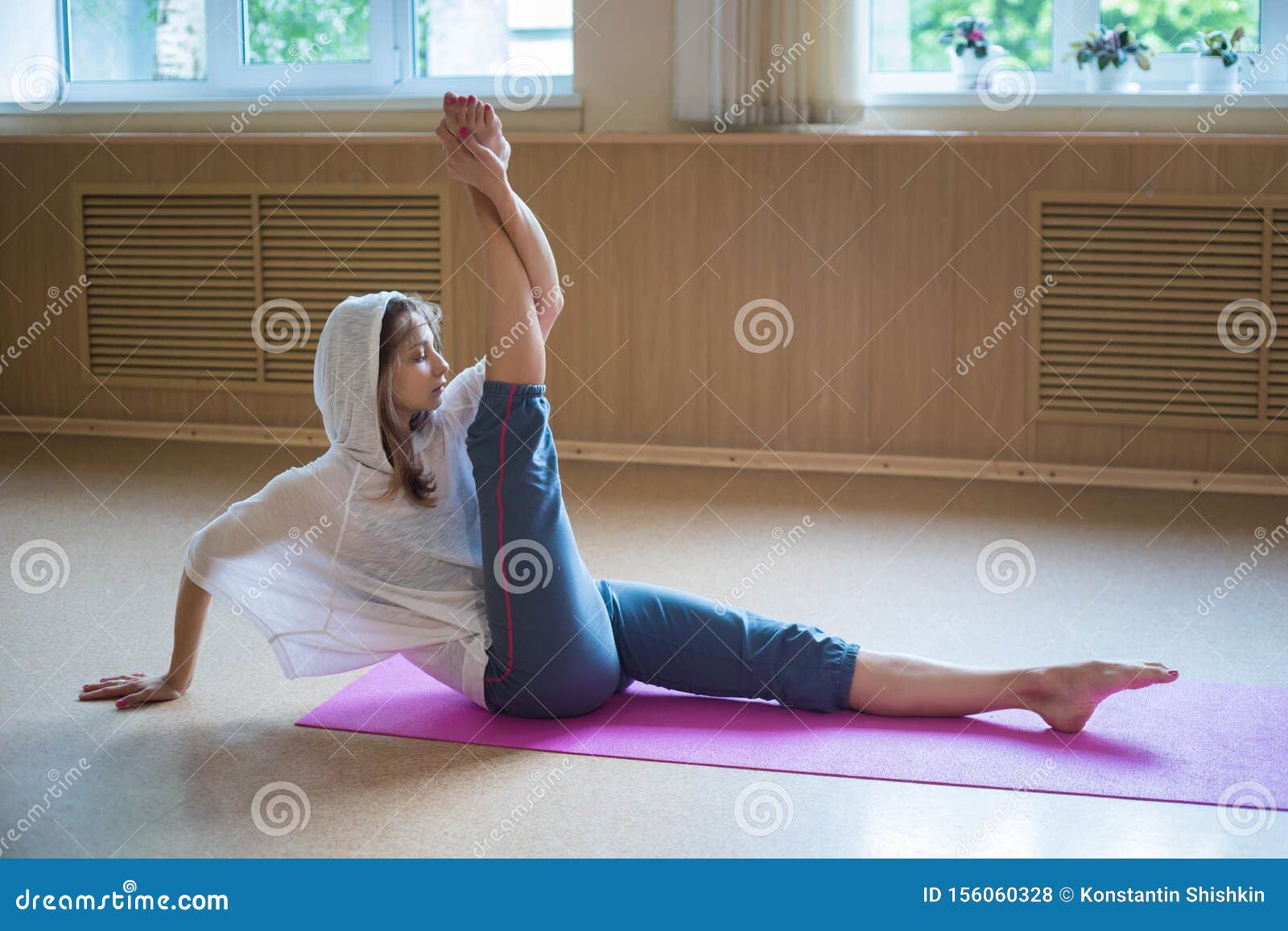 Young Slim Woman in the White Hood Sitting on the Yoga Mat with