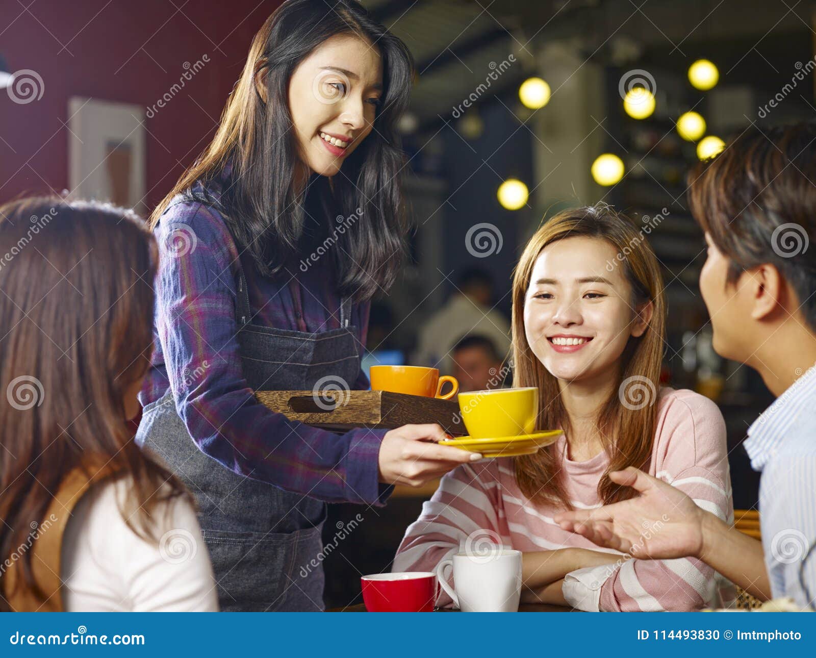 young smiling asian waitress serving coffee to customers