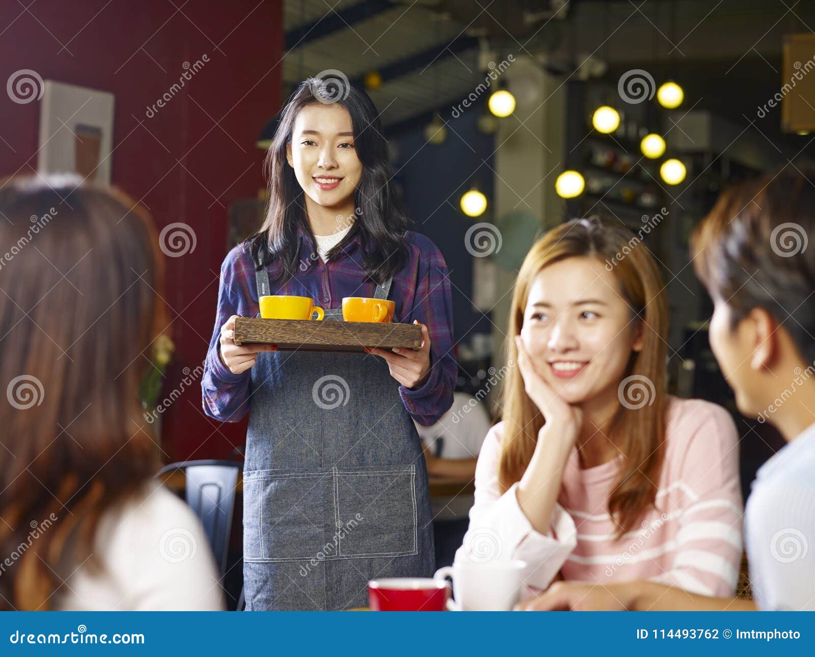 young smiling asian waitress serving coffee to customers