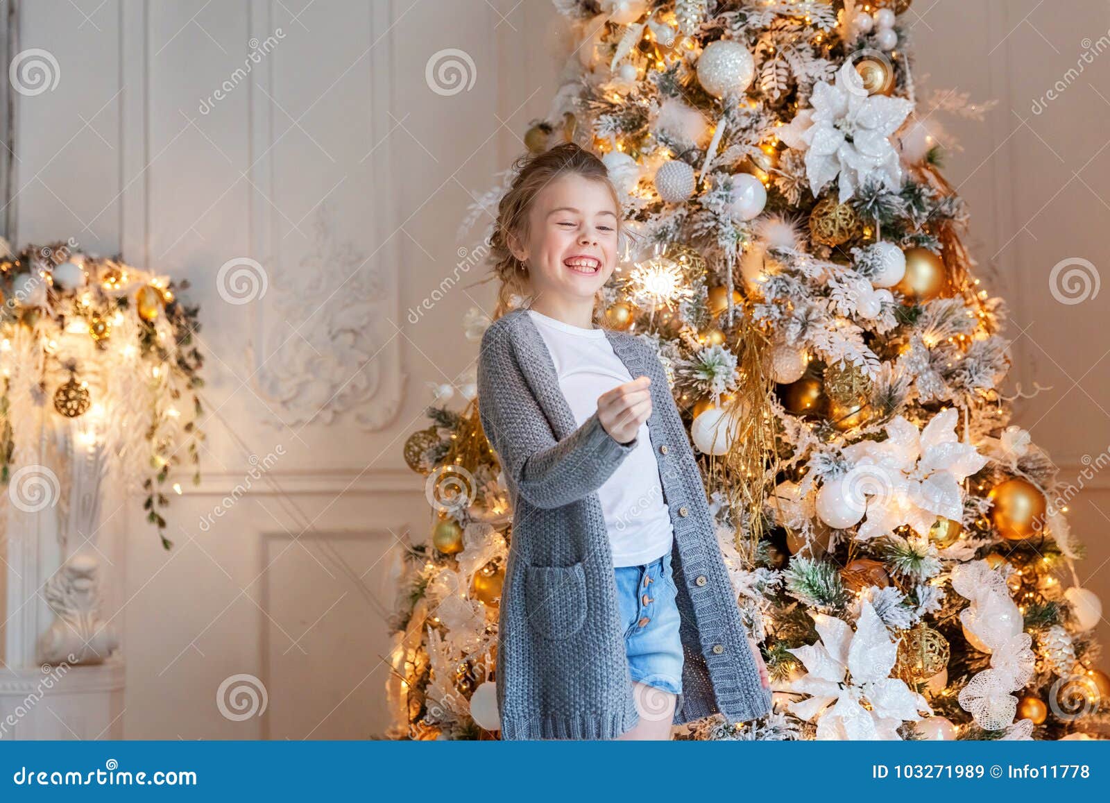 Young smiling beautiful girl with a sparkler under a Christmas tree on Christmas eve at home