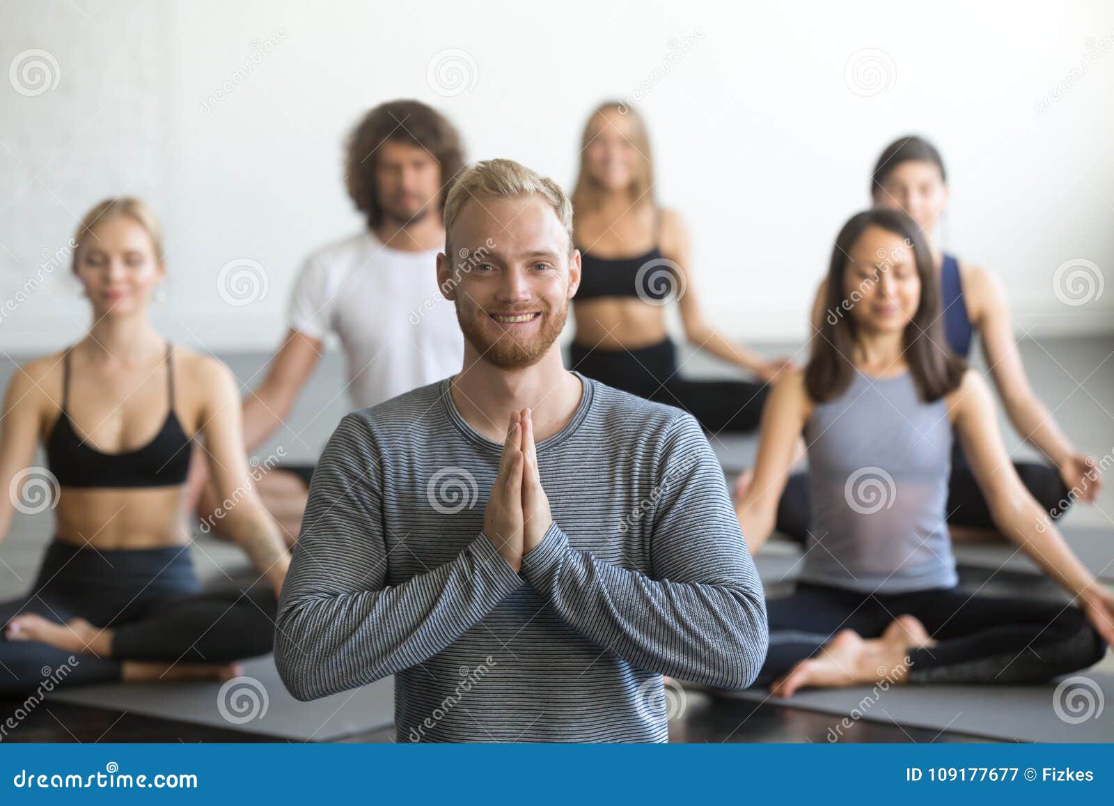 Young Smiling Male Yoga Instructor and Group in Lotus Pose Stock Image