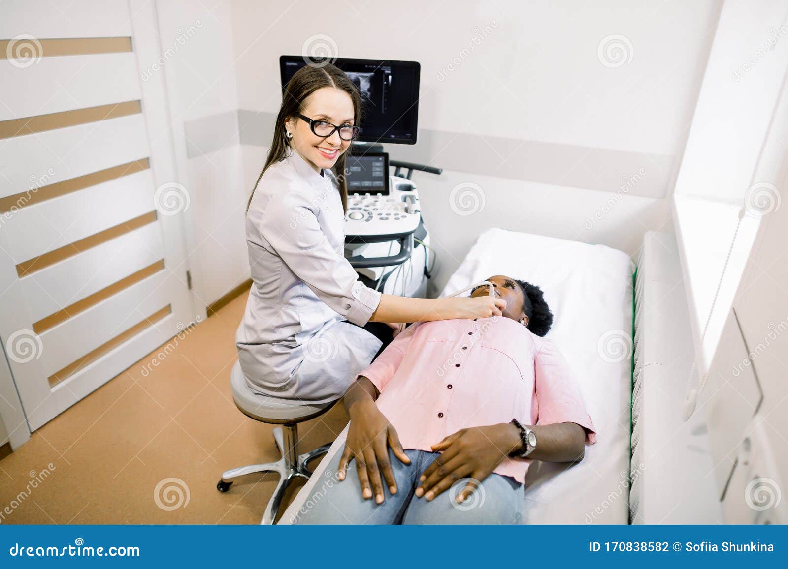 young smiling woman doctor in diagnostic center making ultrasound thyroid gland test to female african patient. woman