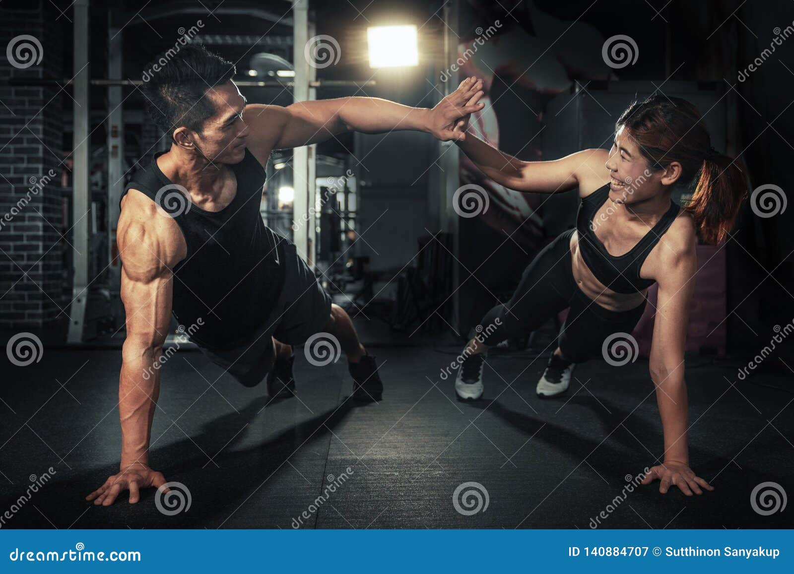 young sporty couple working out together at gym, fitness man and woman giving each other a high five after the training session in