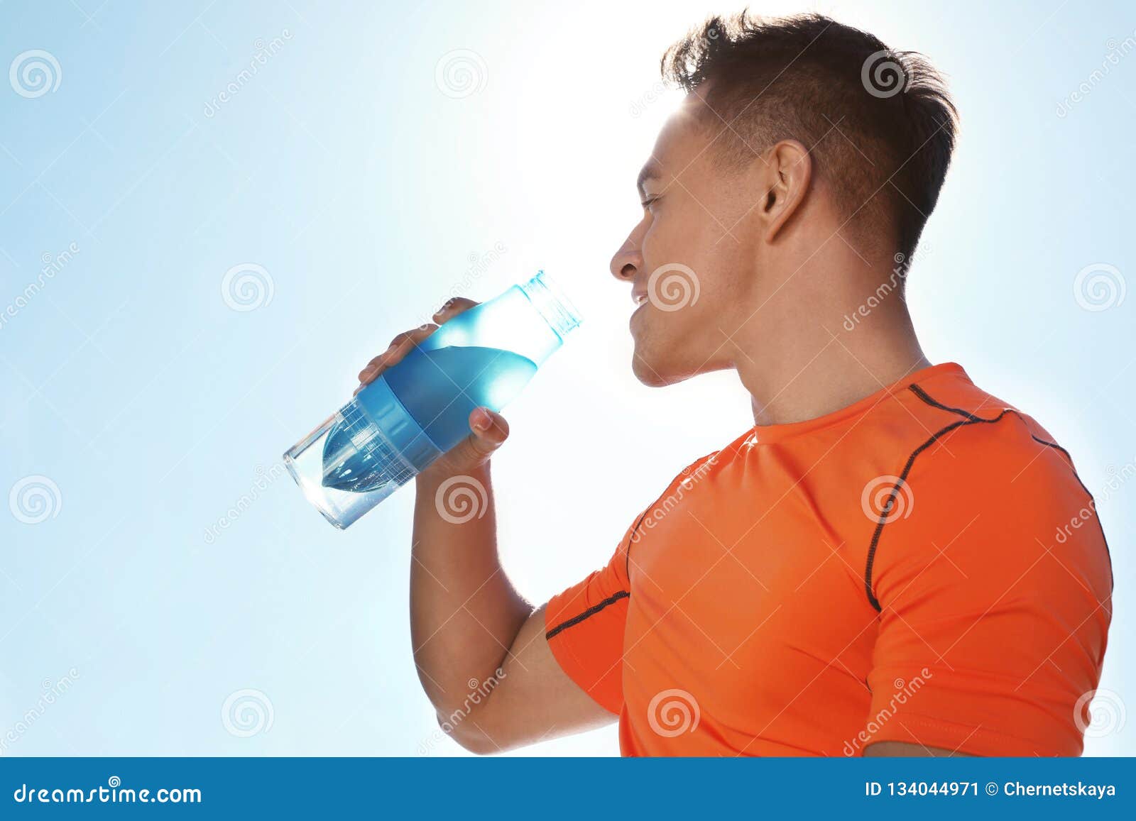 Young Sporty Man Drinking Water from Bottle Against Blue Sky on Sunny ...