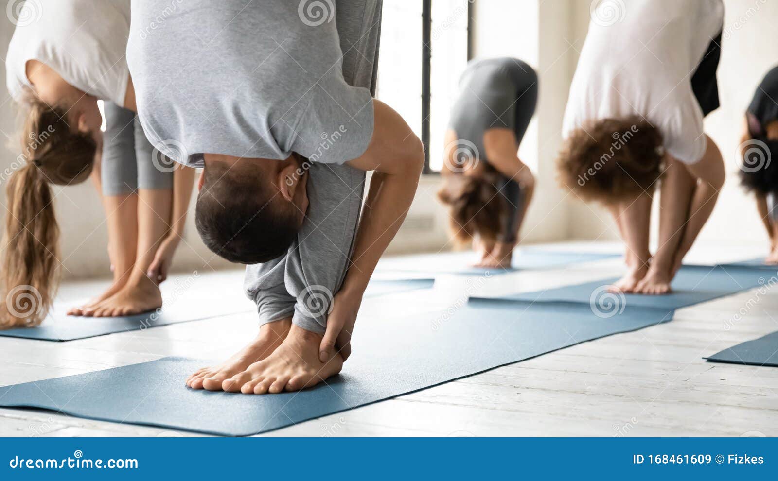 people practicing yoga at group lesson, standing in uttanasana pose