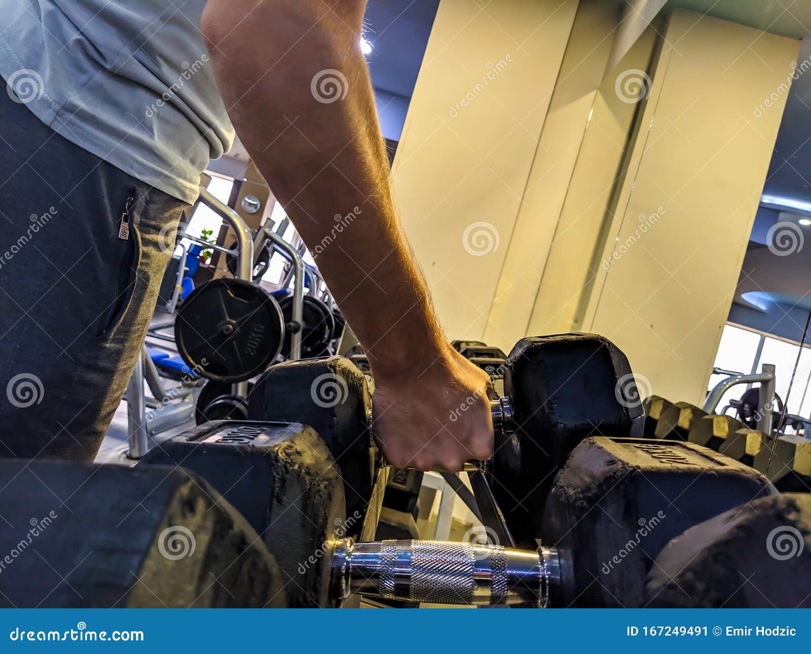 Young Strong Man Hand Picking Up a Metal Weight Dumbbell in a Gym for