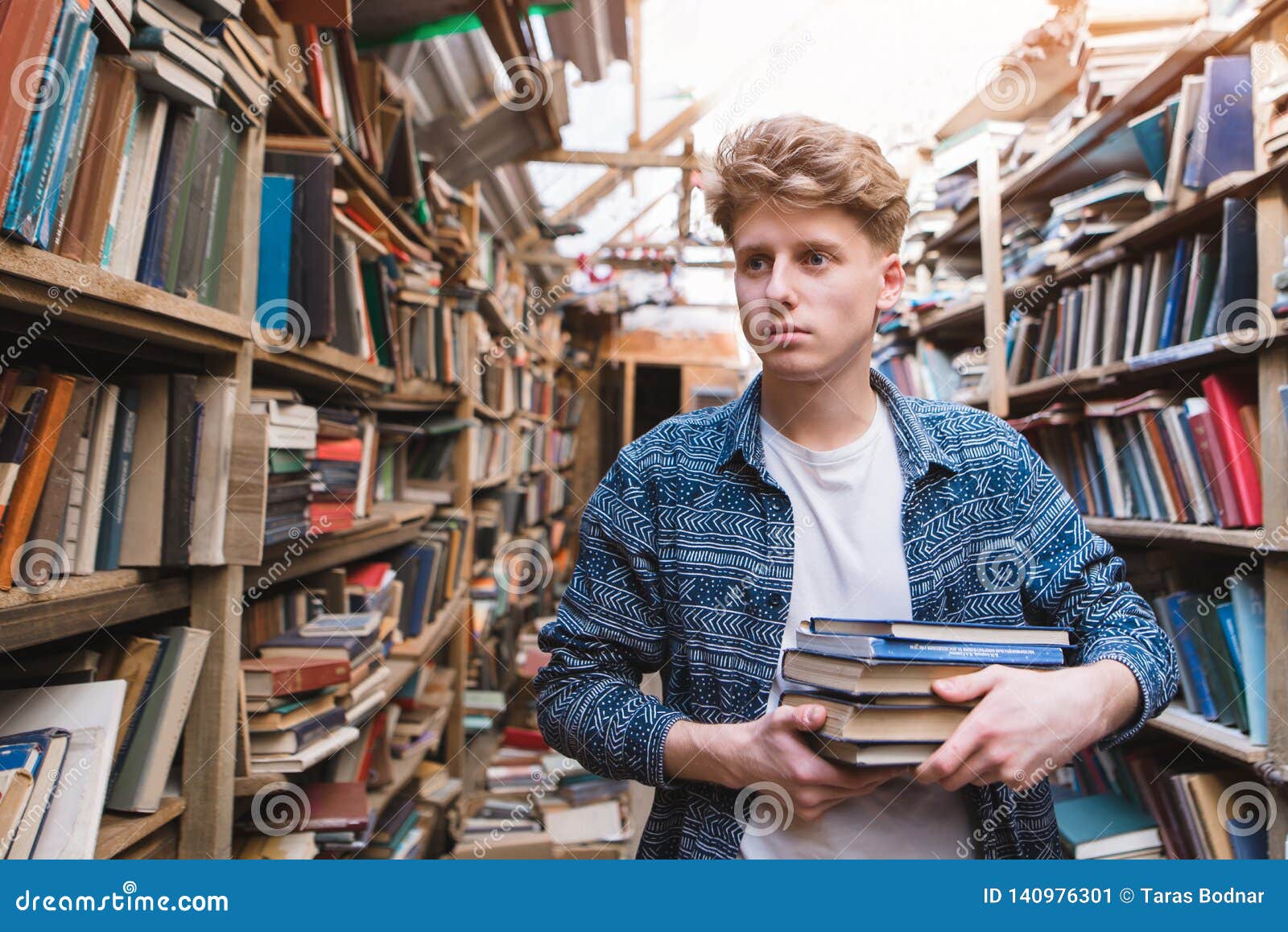 young student walking in a library with books in his hands and looking for literature