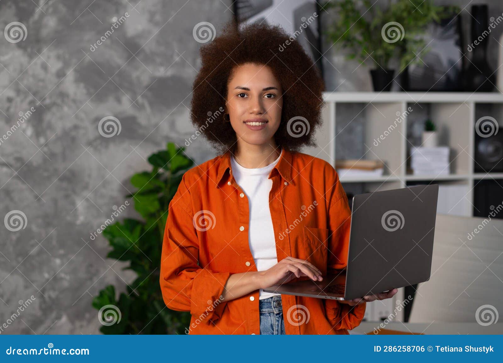 young successful african american woman entrepreneur, ffice worker or ceo working using laptop, stands in modern office or