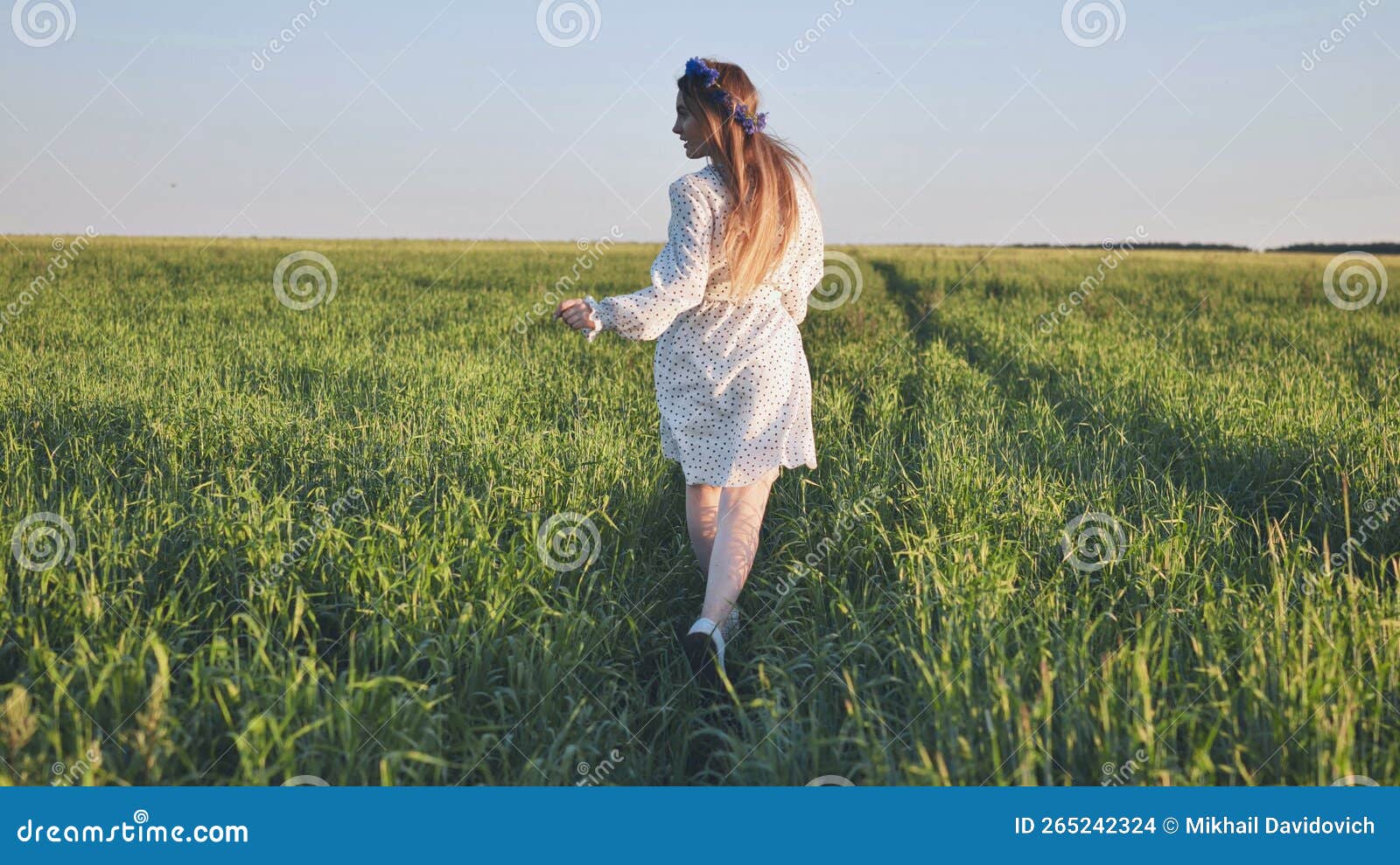 a young ukrainian girl is running through a young wheat field.